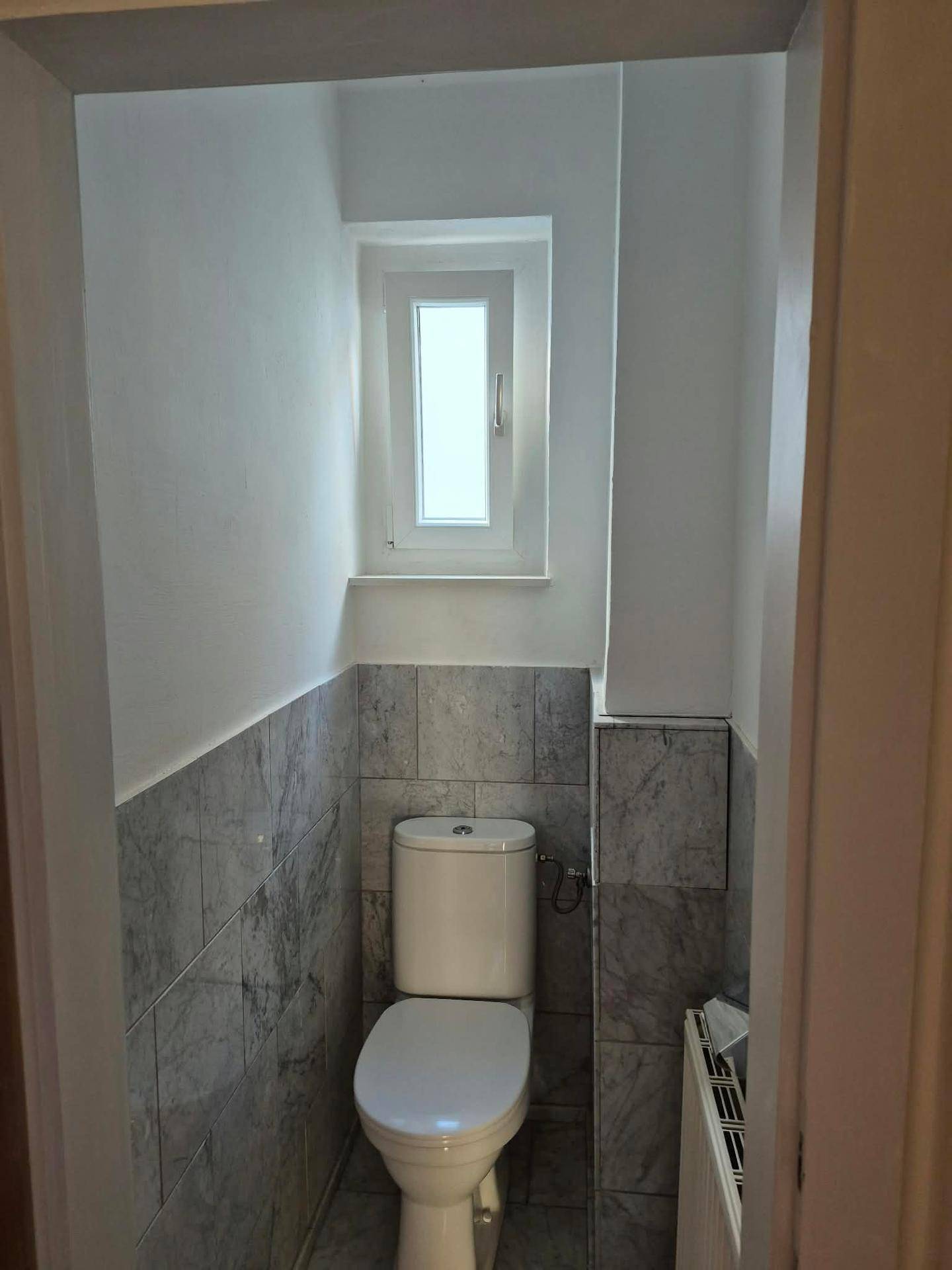 Kleines Gäste-WC mit Toilette, halbhoch gefliesten Wänden und einem kleinen Fenster für Tageslicht.