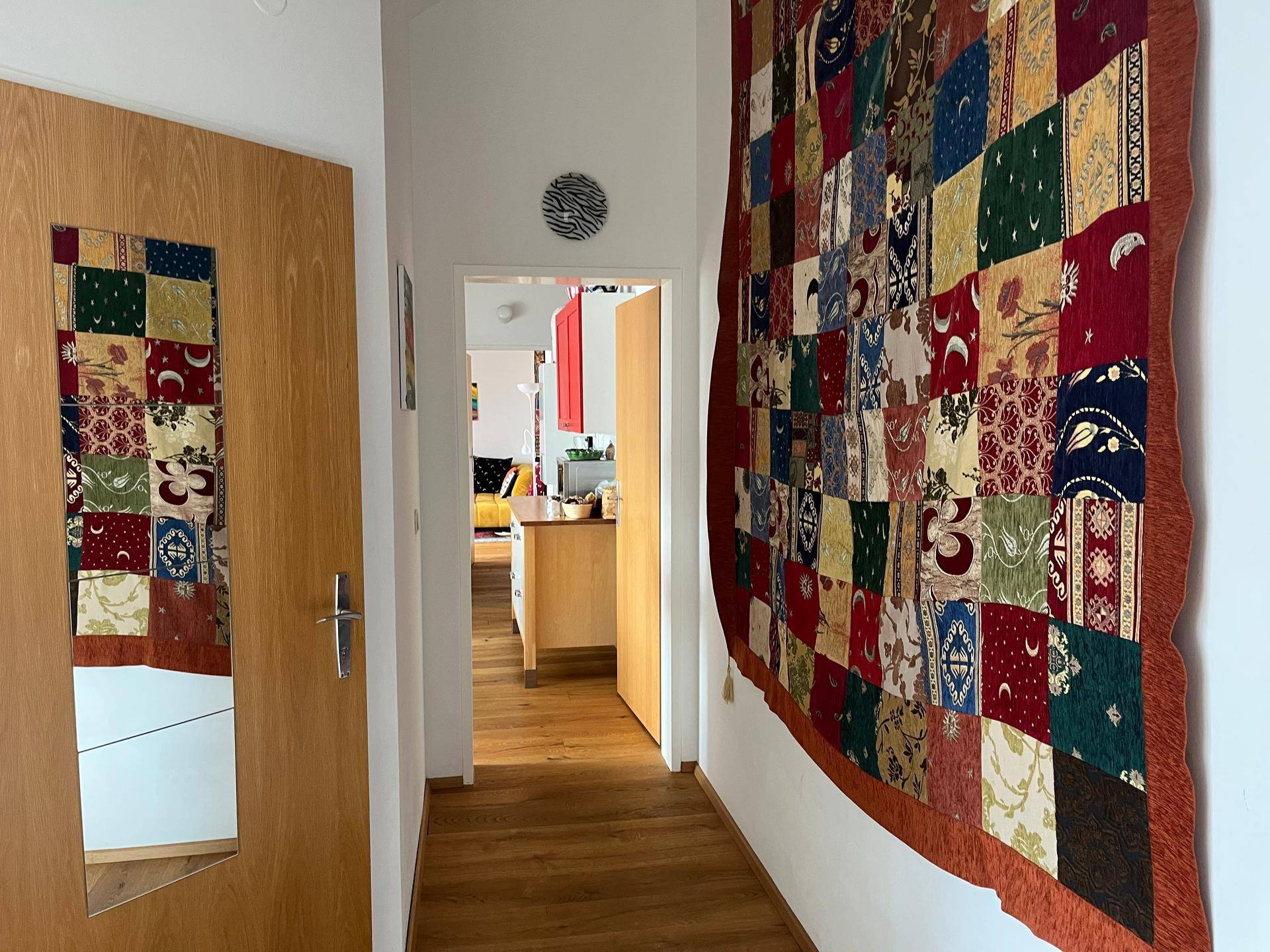 Heller Flur mit Holzboden, farbenfrohem Wandteppich und Zugang zu weiteren Räumen der Wohnung.