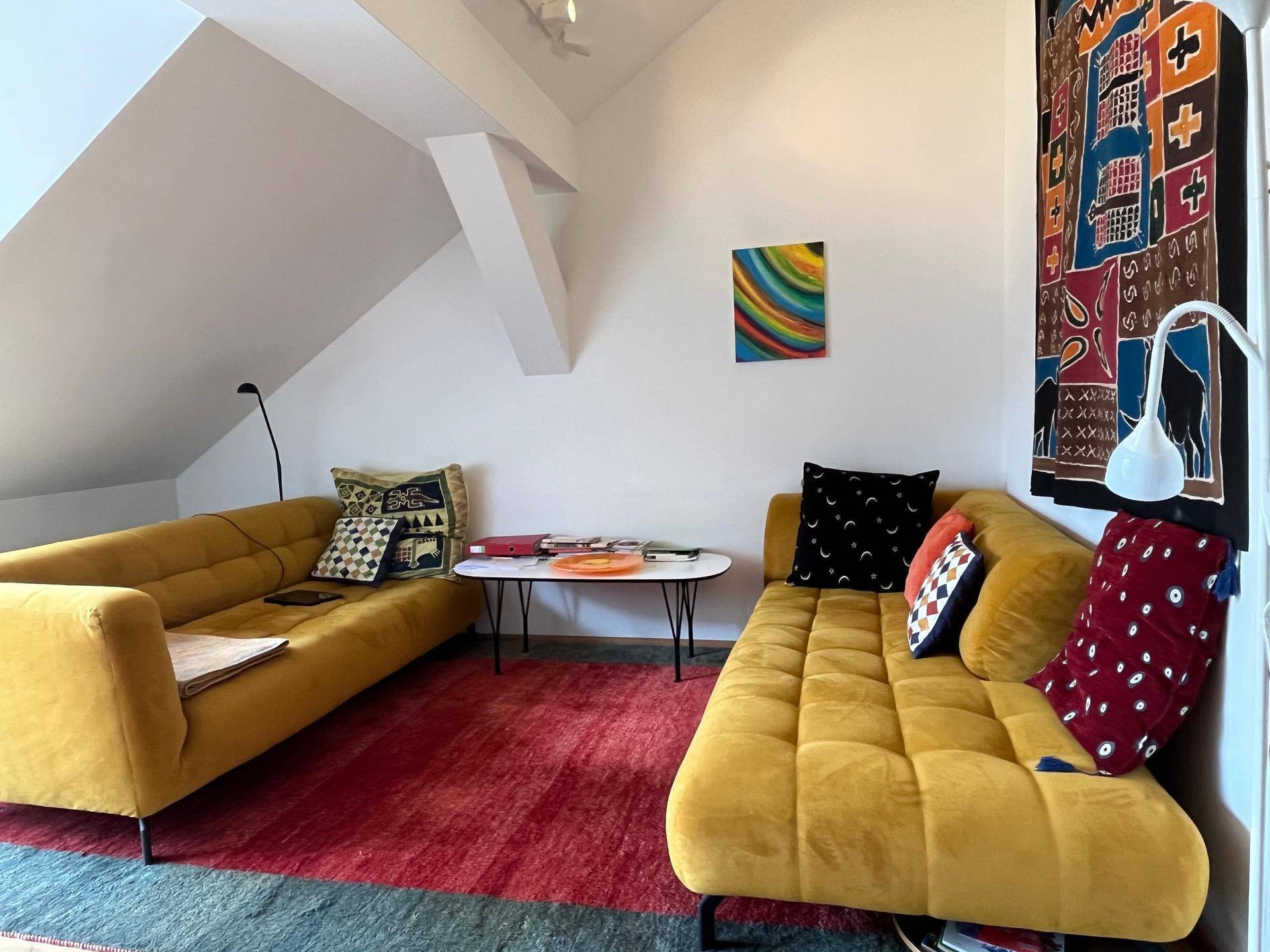 Gemütliches Wohnzimmer mit zwei gelben Sofas, Couchtisch und farbenfroher Kunst an den Wänden.