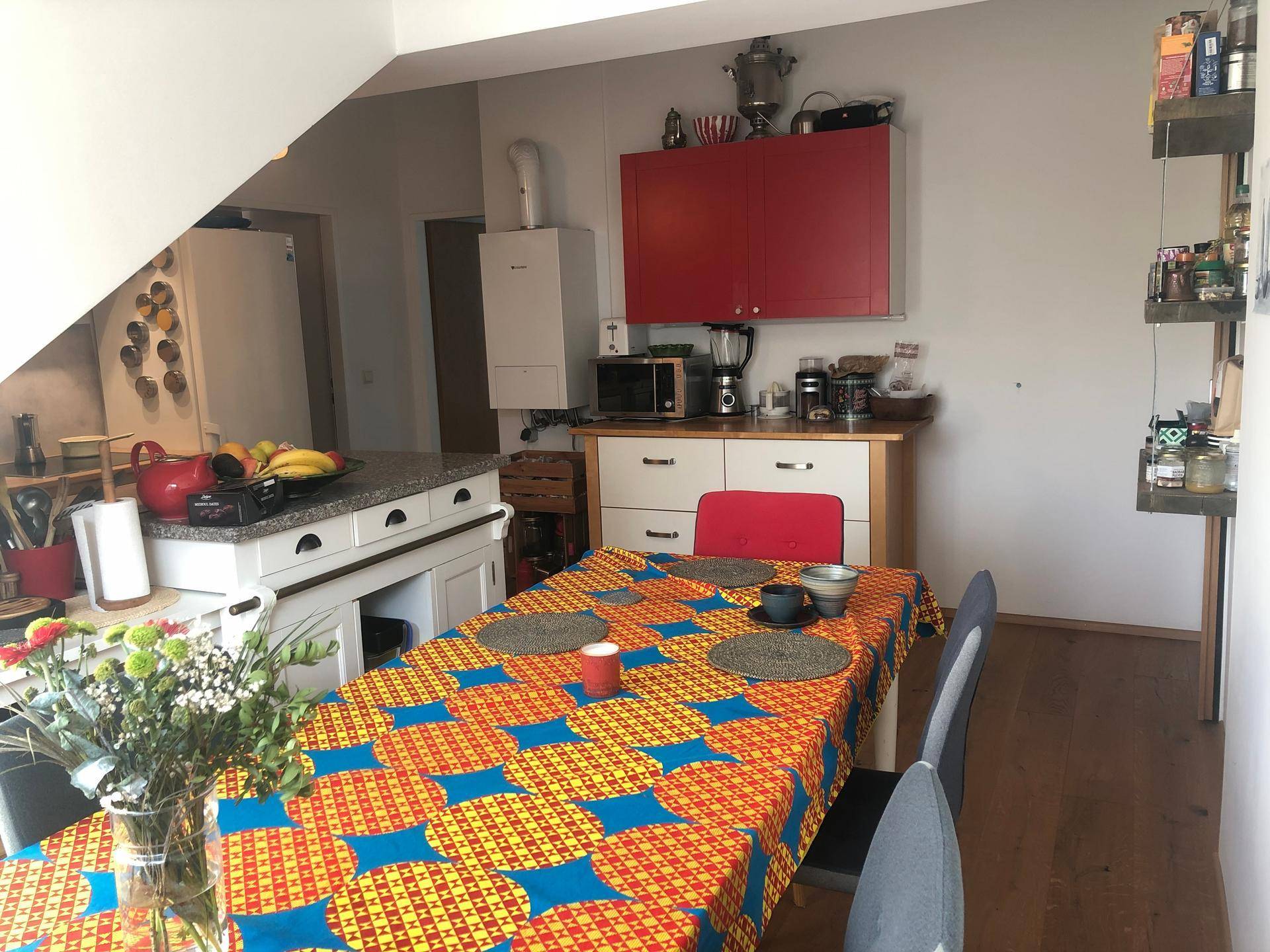 Funktionale Küche mit Essbereich, roten Hängeschränken, Kühlschrank und Dachschrägen.