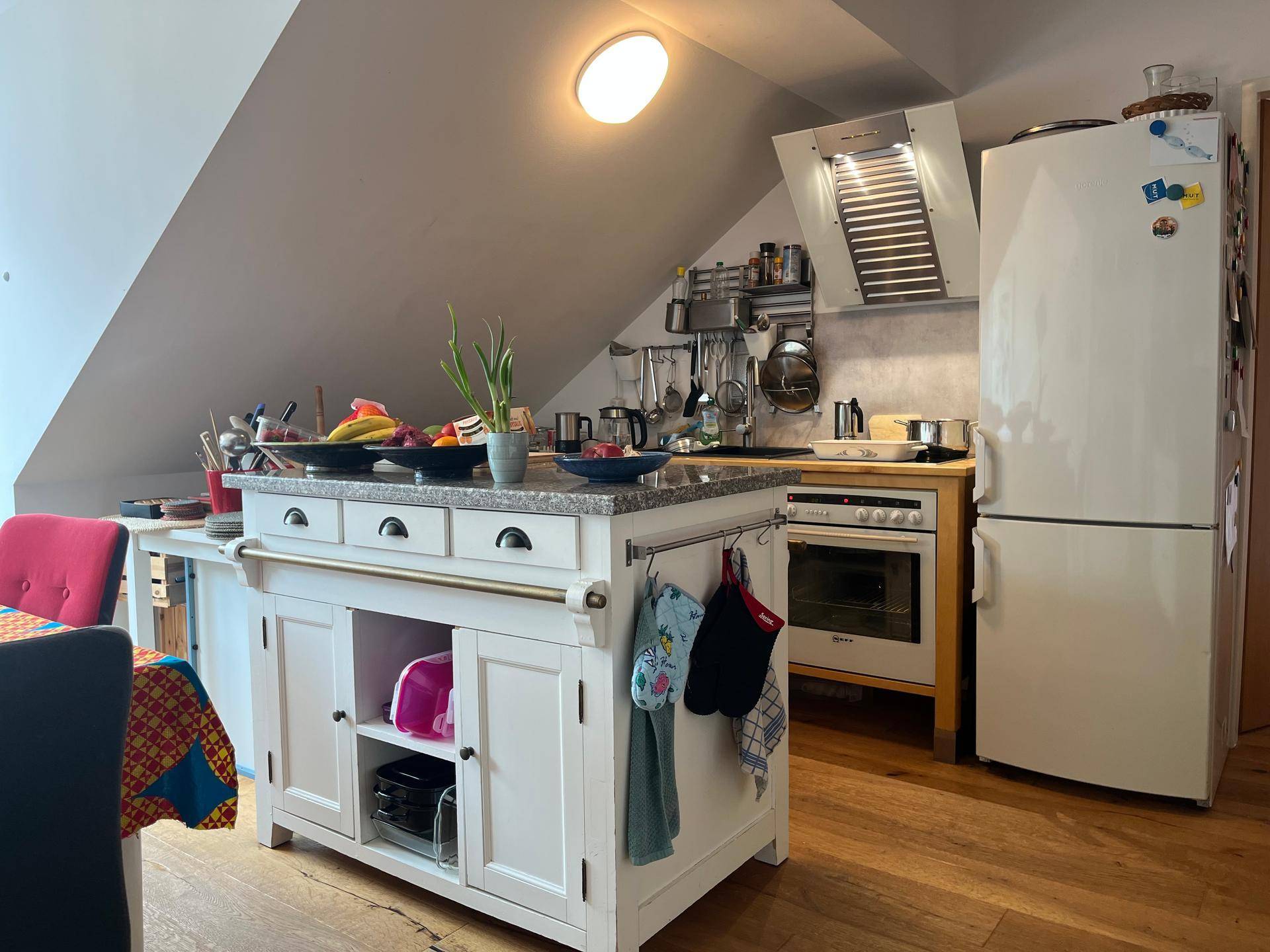 Praktische Küche mit Kücheninsel, Backofen, Dunstabzugshaube und großem Kühlschrank unter der Dachschräge.