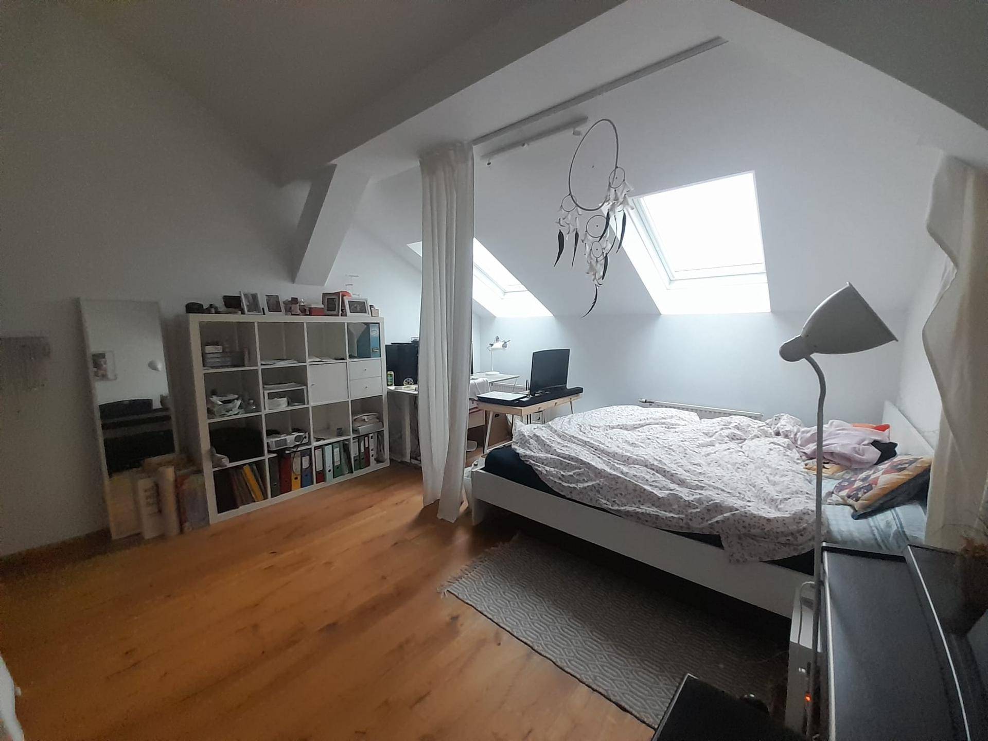 Helles Schlafzimmer im Dachgeschoss mit schrägen Wänden, Dachfenstern und integriertem Arbeitsbereich.
