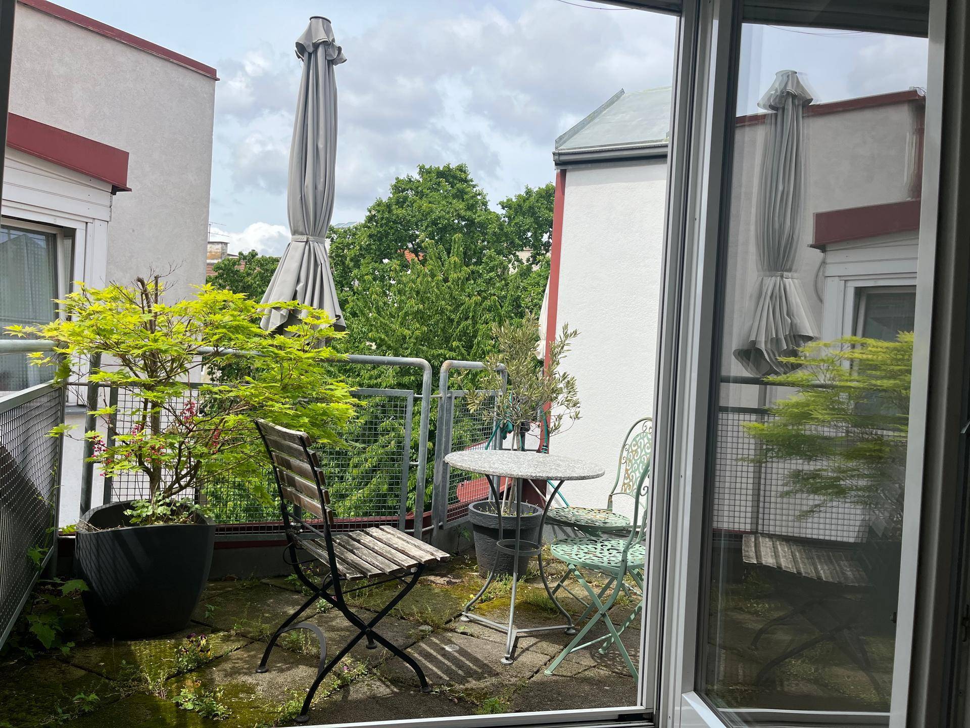 Balkon mit Sitzgelegenheiten und Topfpflanzen, umgeben von Bäumen und mit Blick auf die Umgebung.