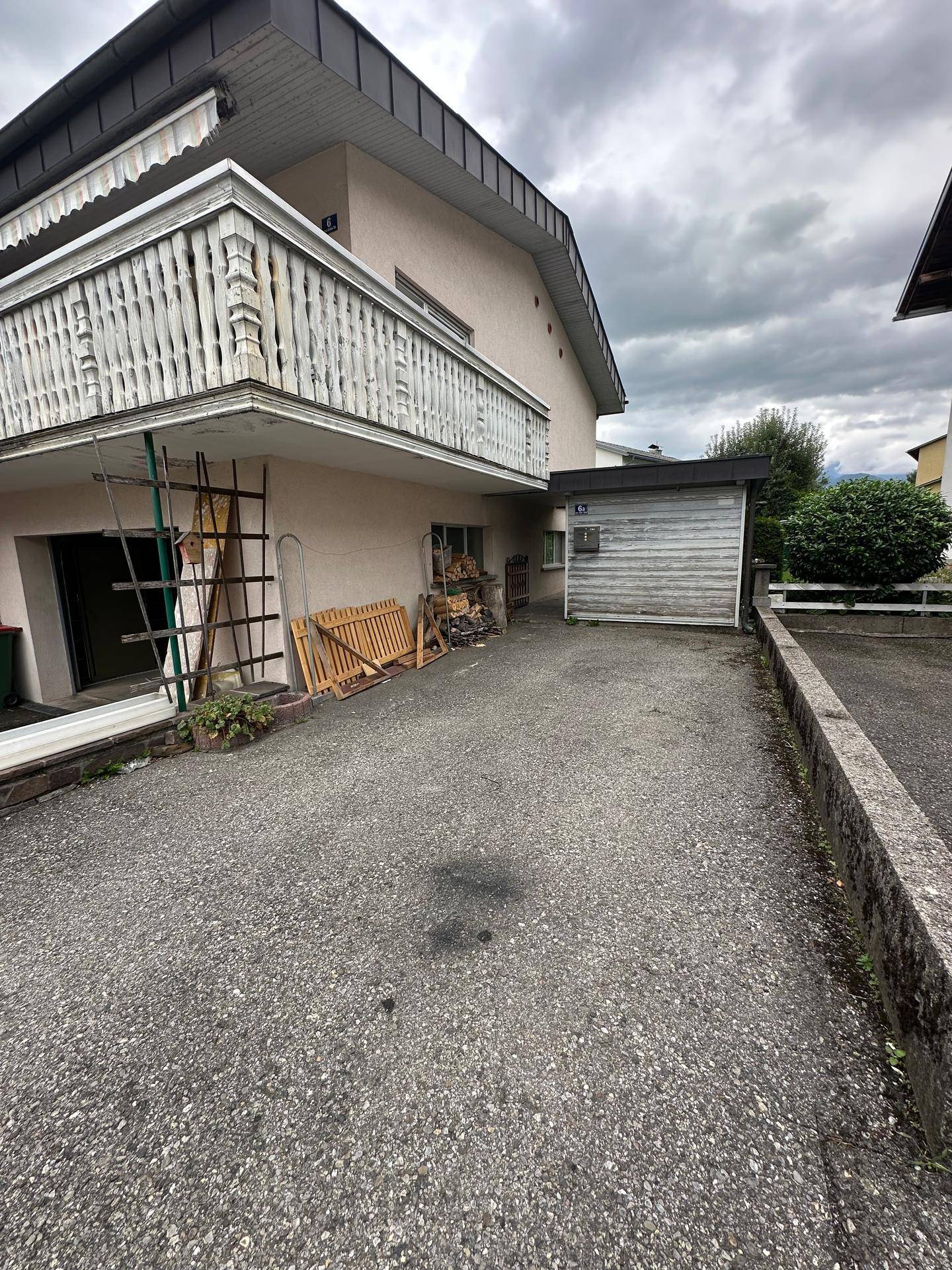 Ansicht des Hauses mit Balkon, Garage und Zufahrt unter bewölktem Himmel.