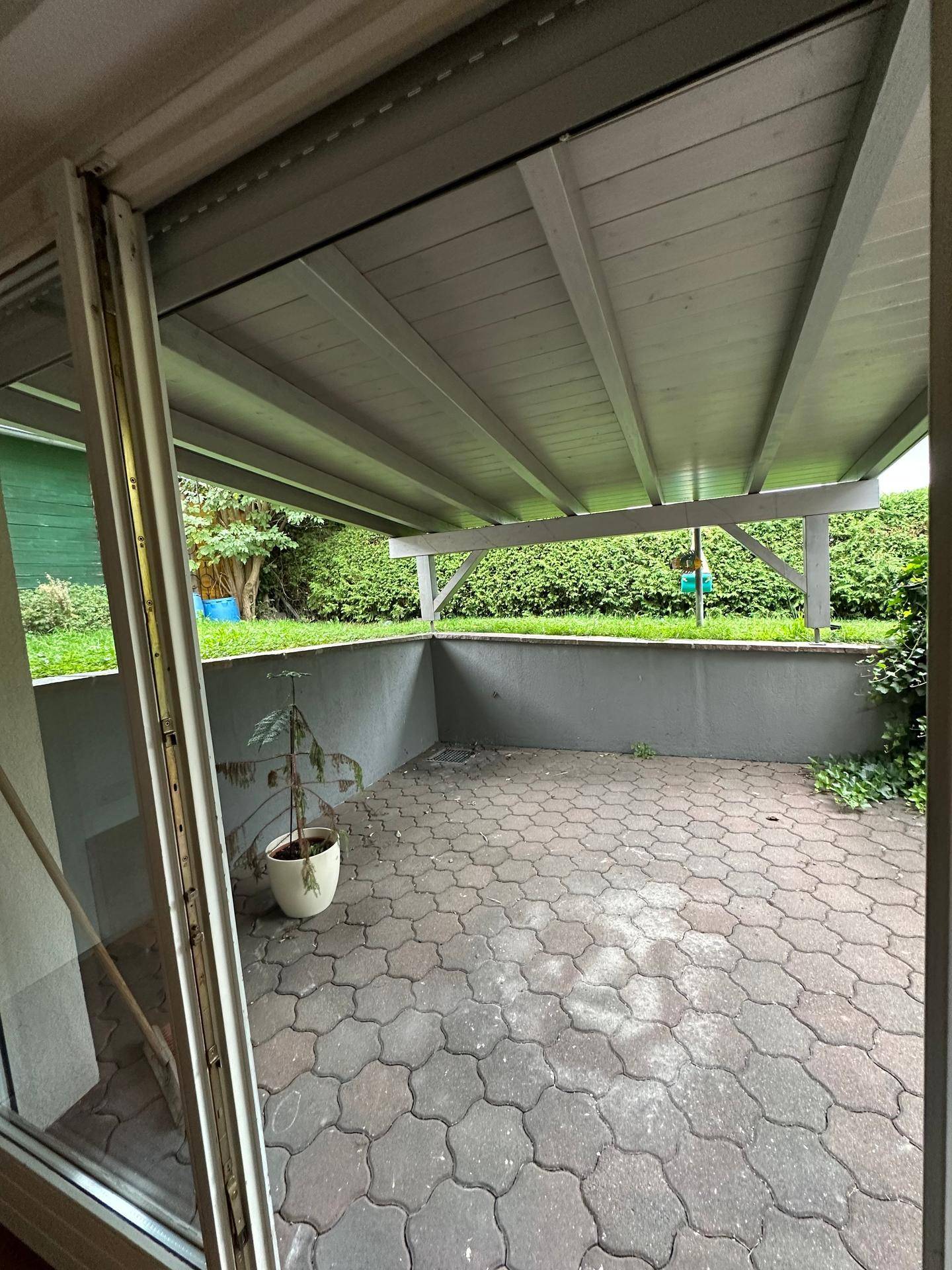 Überdachte Terrasse mit Pflastersteinen und Blick auf den grünen Gartenbereich.