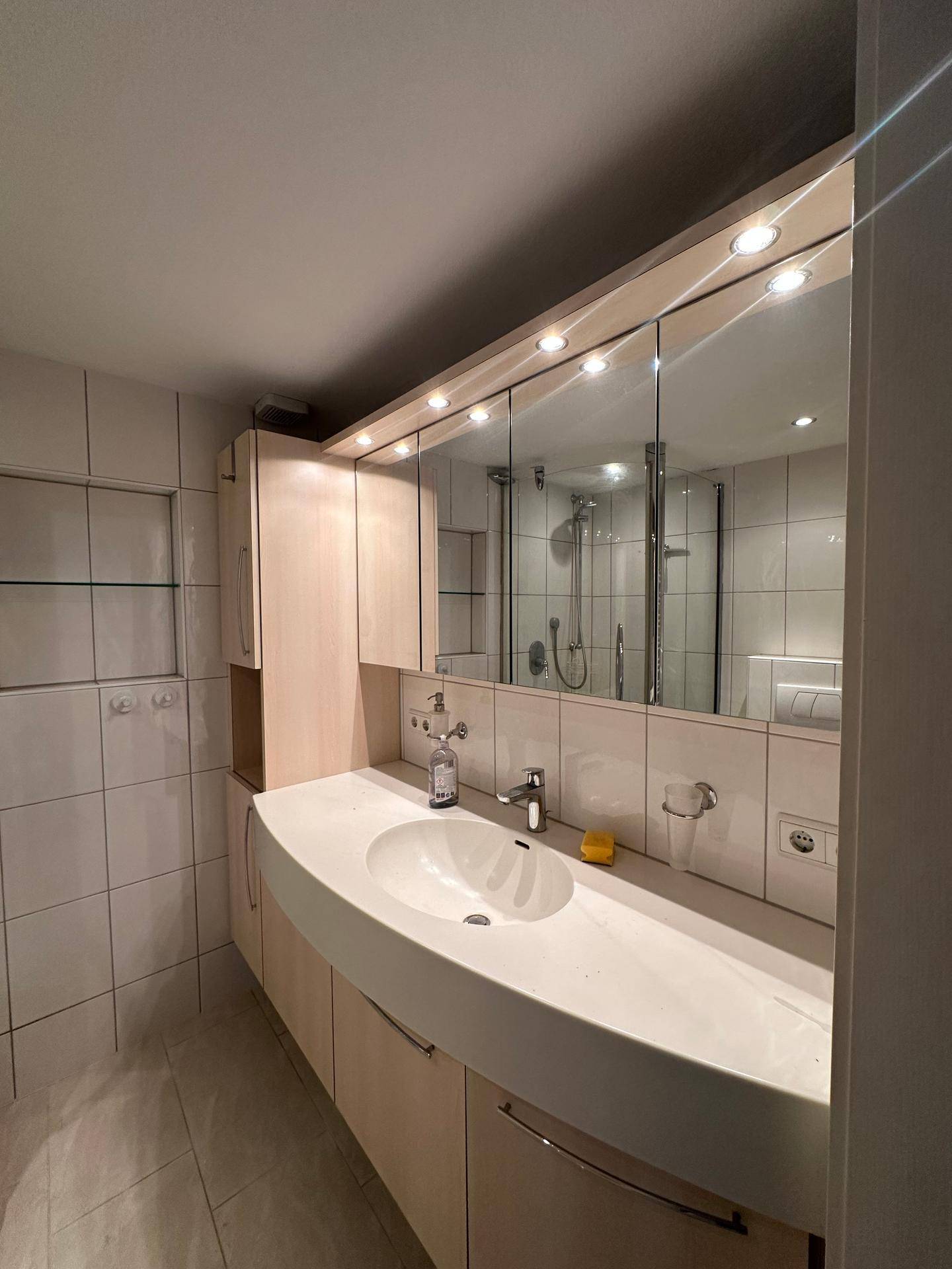 Badezimmer mit großem Einzelwaschbecken, Spiegelschrank und integrierter Beleuchtung.