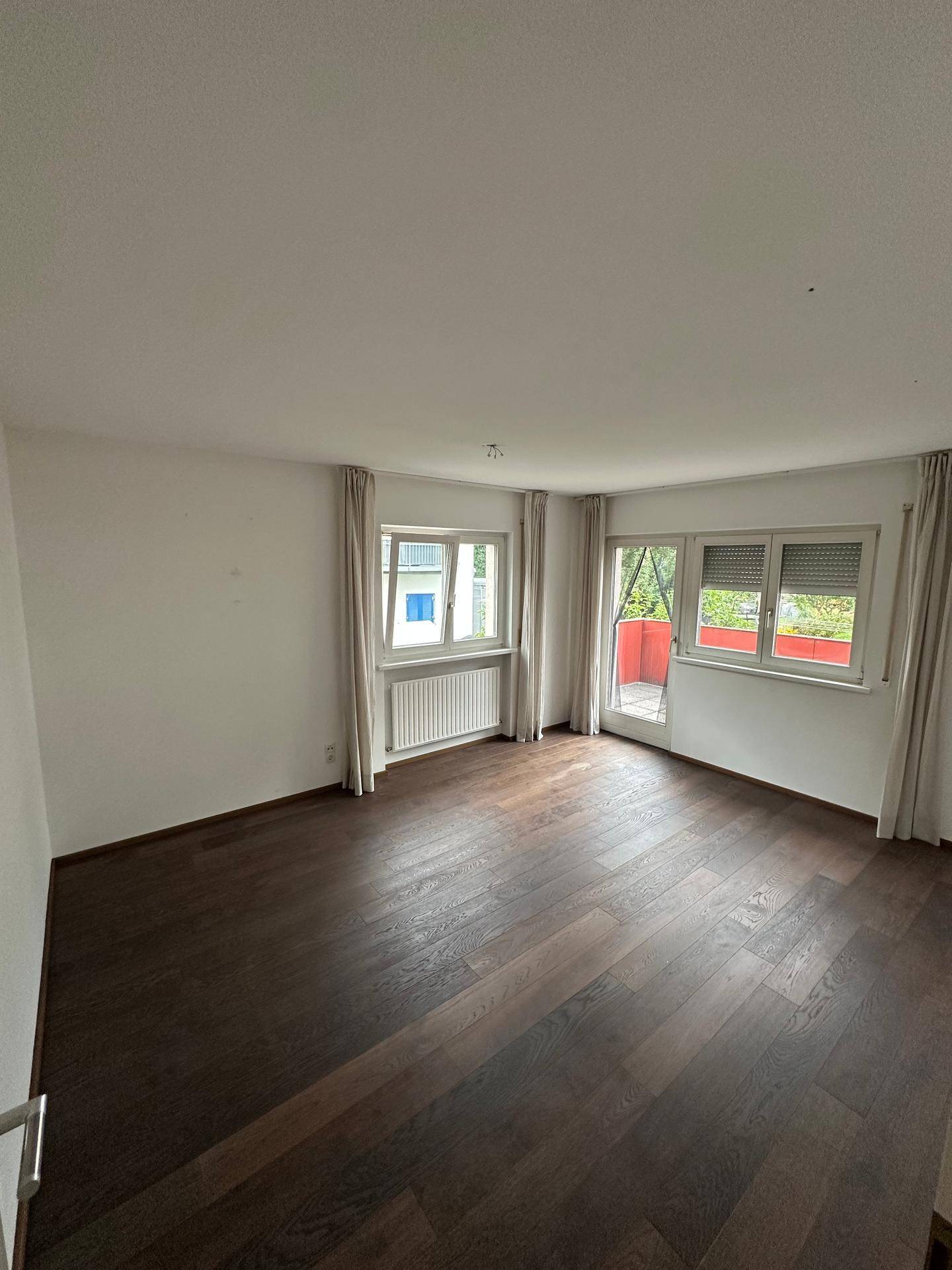 Helles Schlafzimmer mit dunklem Holzboden und Zugang zu einem kleinen Balkon.