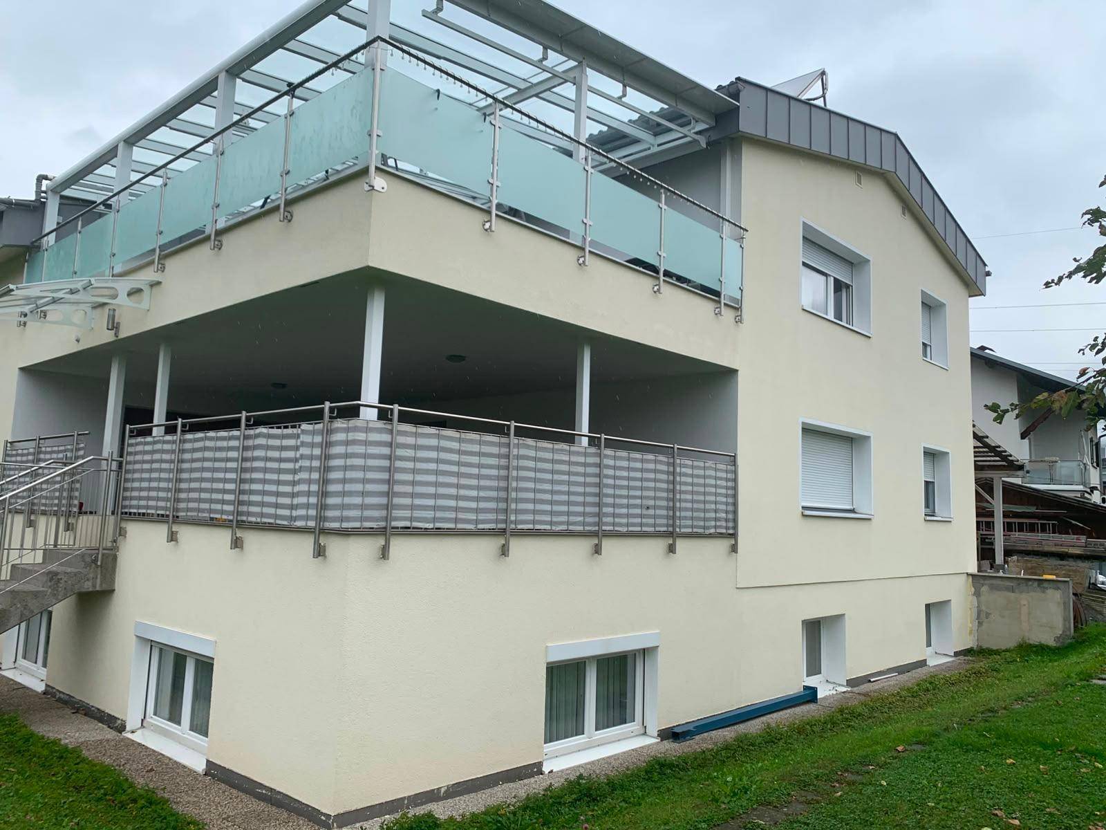 Seitenansicht des modernen Gebäudes mit mehreren überdachten Balkonen, Glasgeländern und Grünblick.