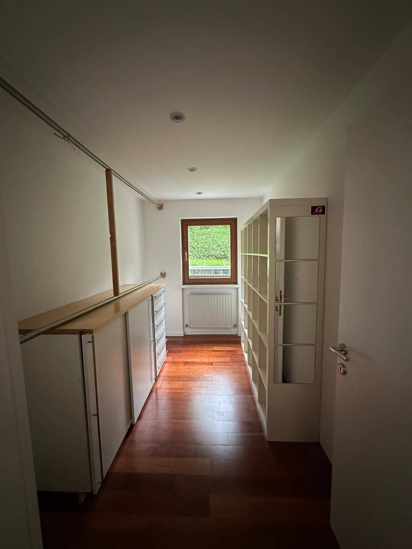 Langer Raum mit Holzboden, Regalen und Fenster, ideal als Abstell- oder Hobbyraum.