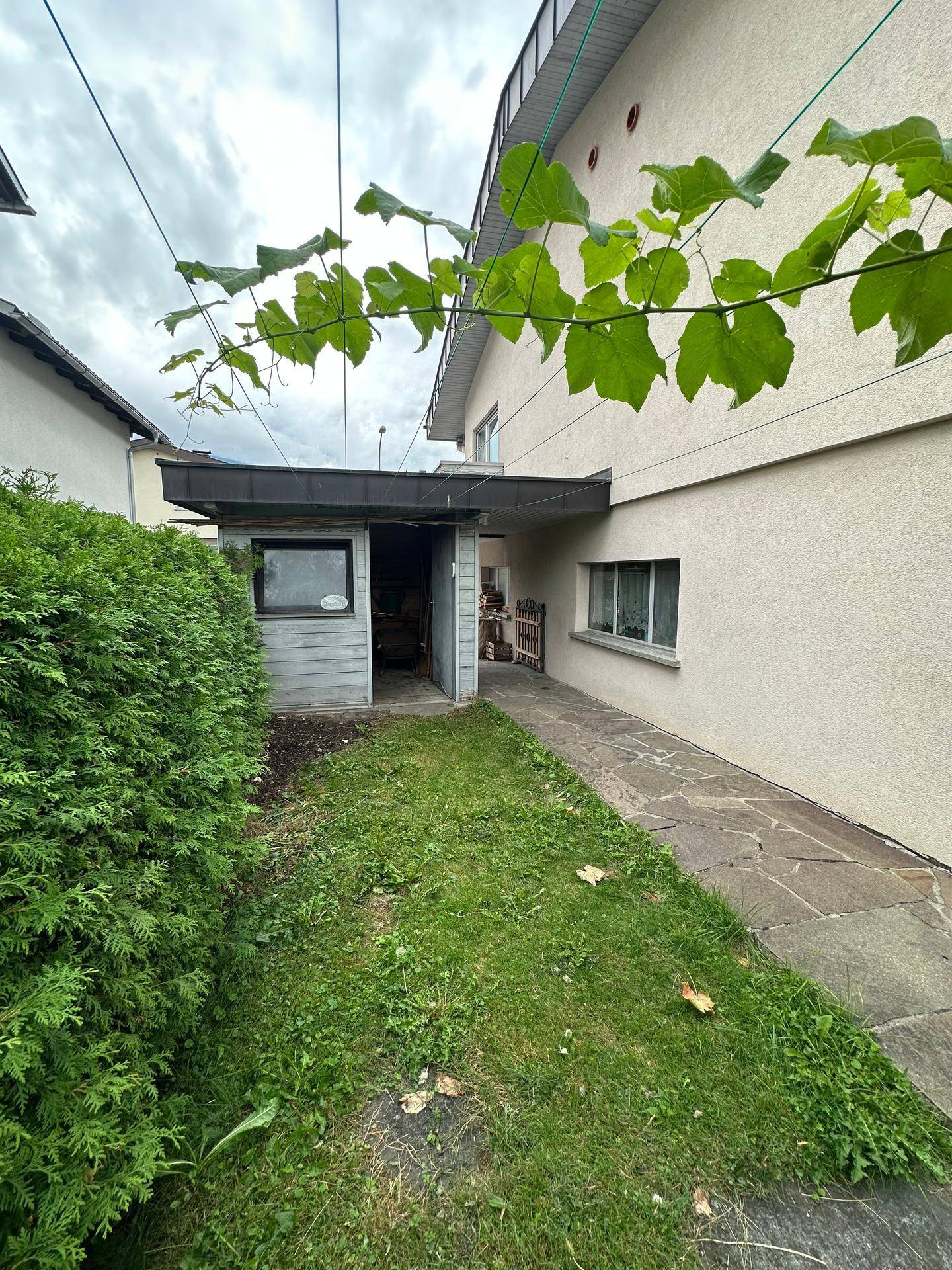 Seitlicher Gartenbereich mit Rasenfläche, Hecke und einem kleinen Schuppen.