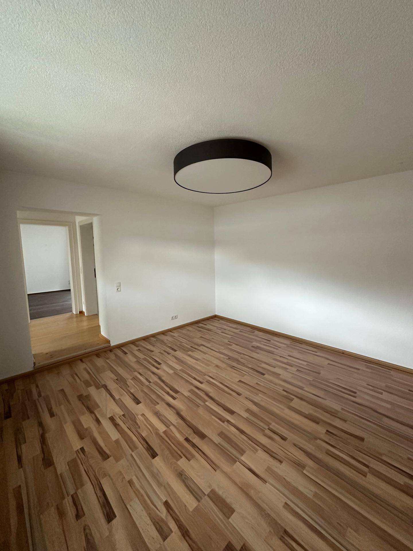Helles Schlafzimmer mit Holzboden und Zugang zu einem weiteren Raum.