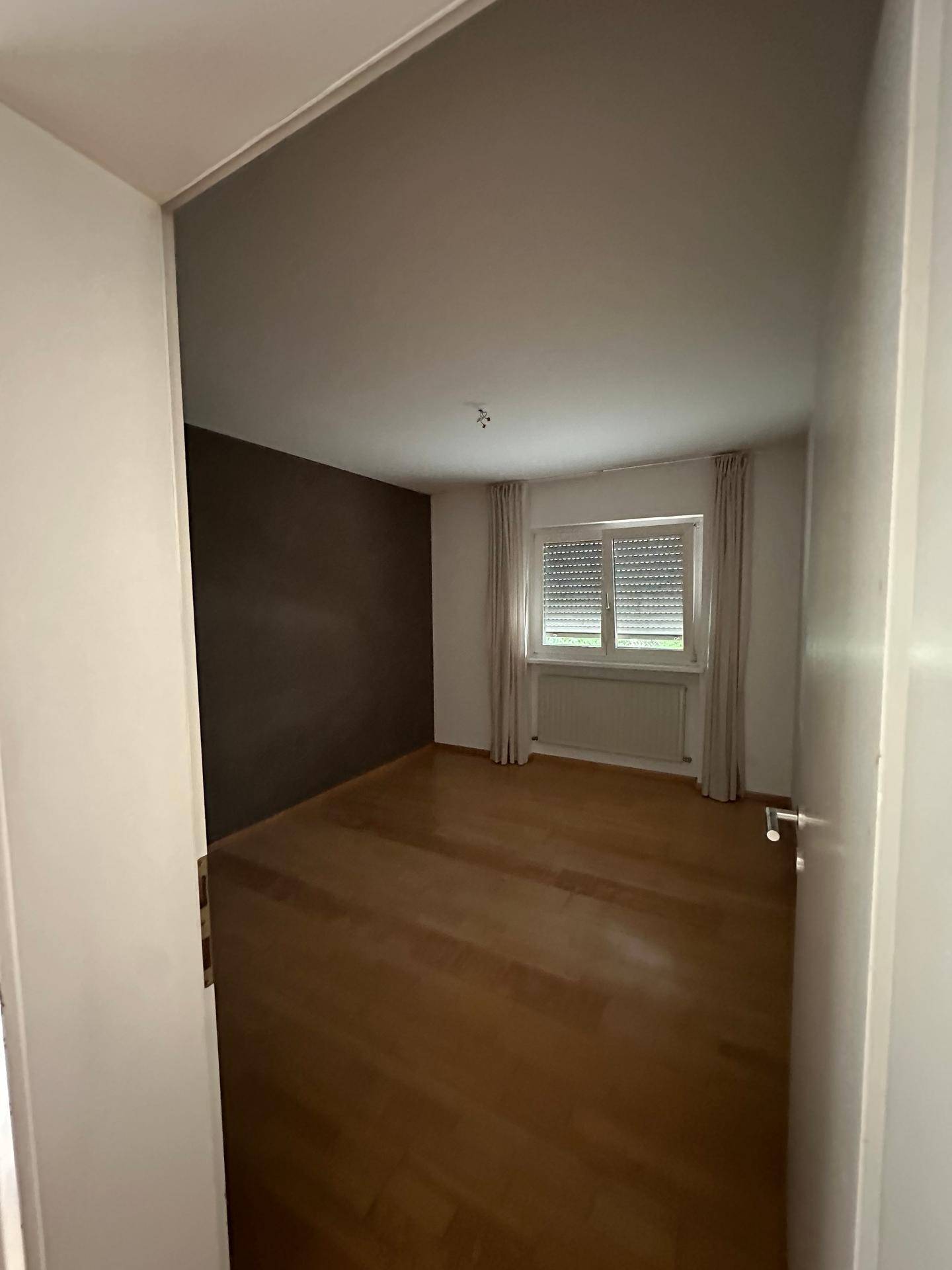 Schlafzimmer mit Holzboden, dunkler Akzentwand und Fenster mit Rollladen.