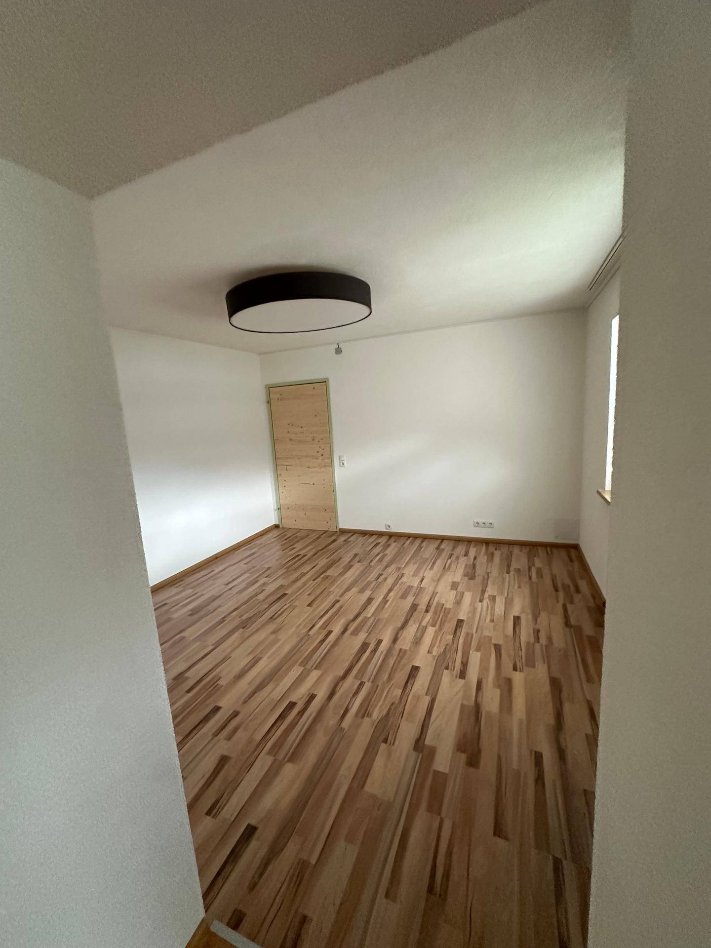 Geräumiges Schlafzimmer mit hellem Holzboden und einer modernen Deckenleuchte.