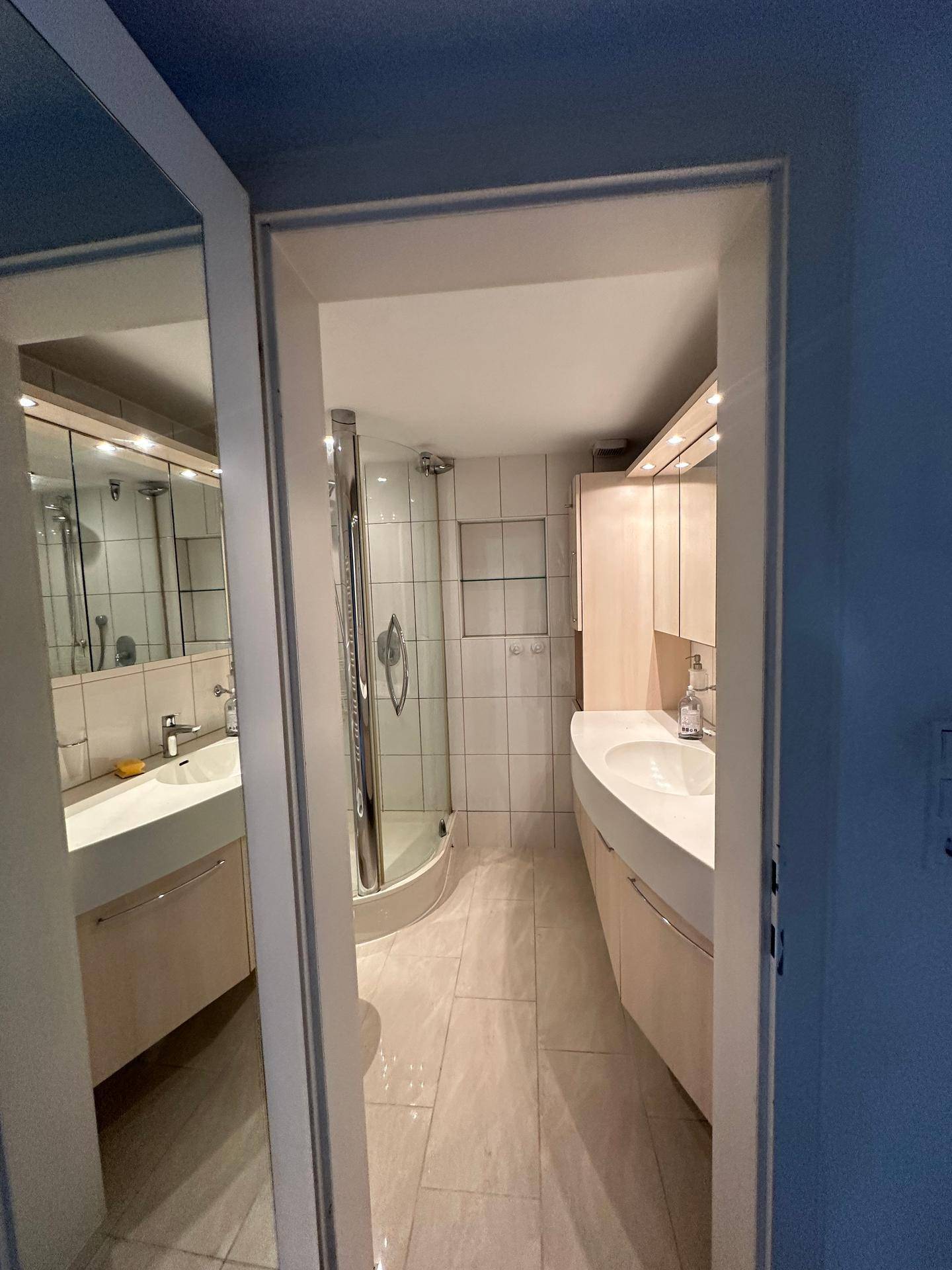 Modernes Badezimmer mit hellem Fliesenboden, Doppelwaschbecken und Duschkabine.