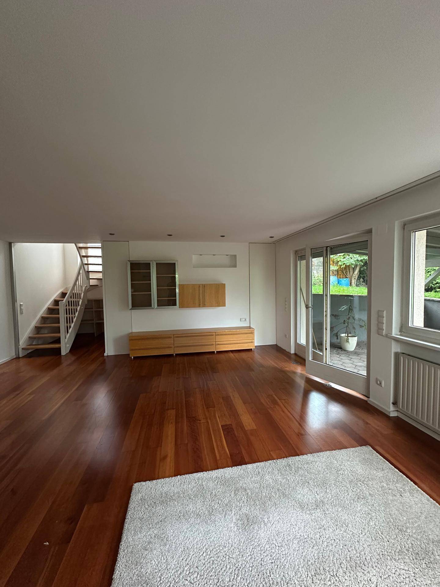 Großzügiges Wohnzimmer mit Holzboden, Einbauschränken und Zugang zur Terrasse.
