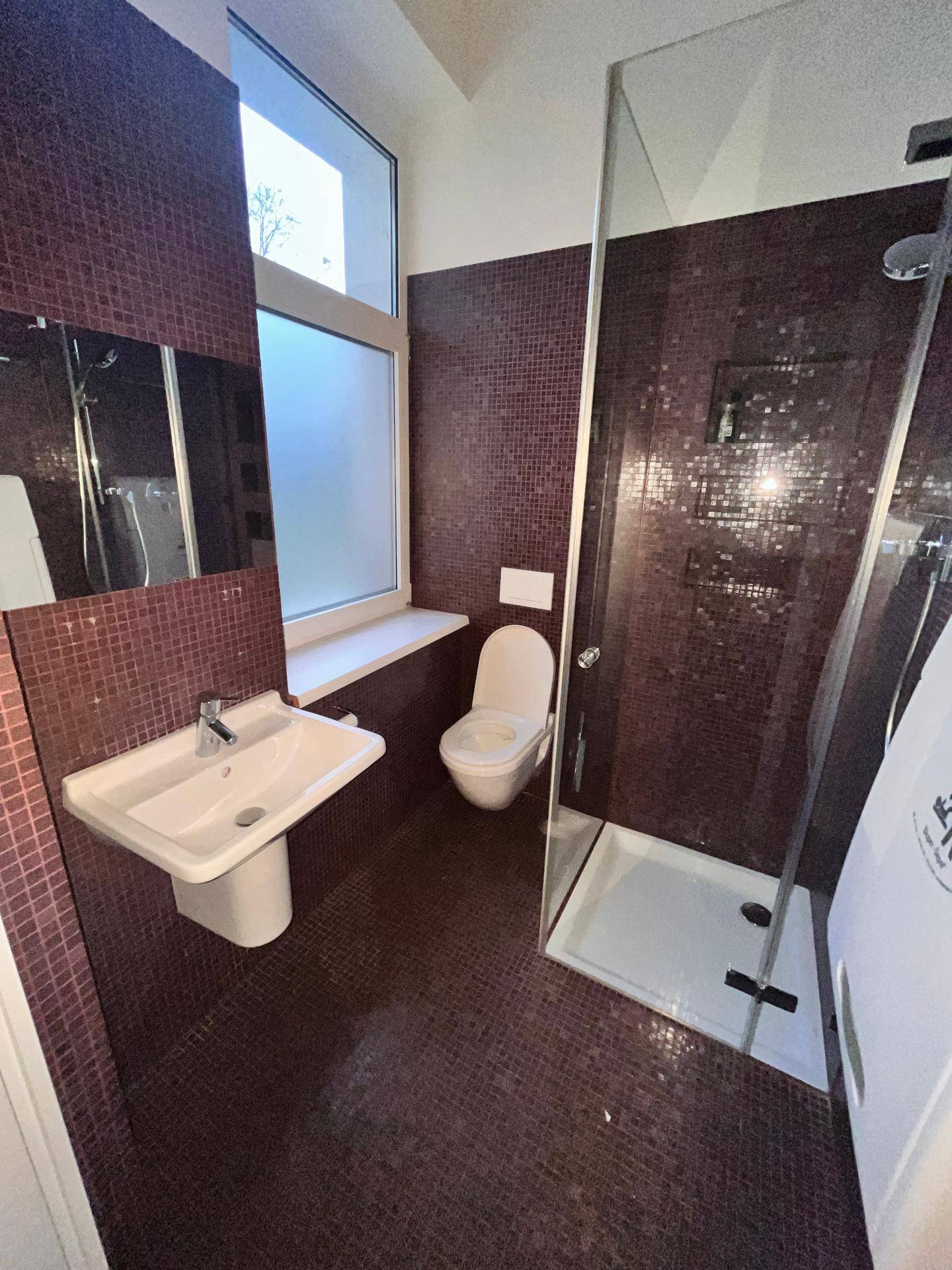 Modernes Badezimmer mit lila Mosaikfliesen, Dusche, WC und Fenster für natürliches Licht.