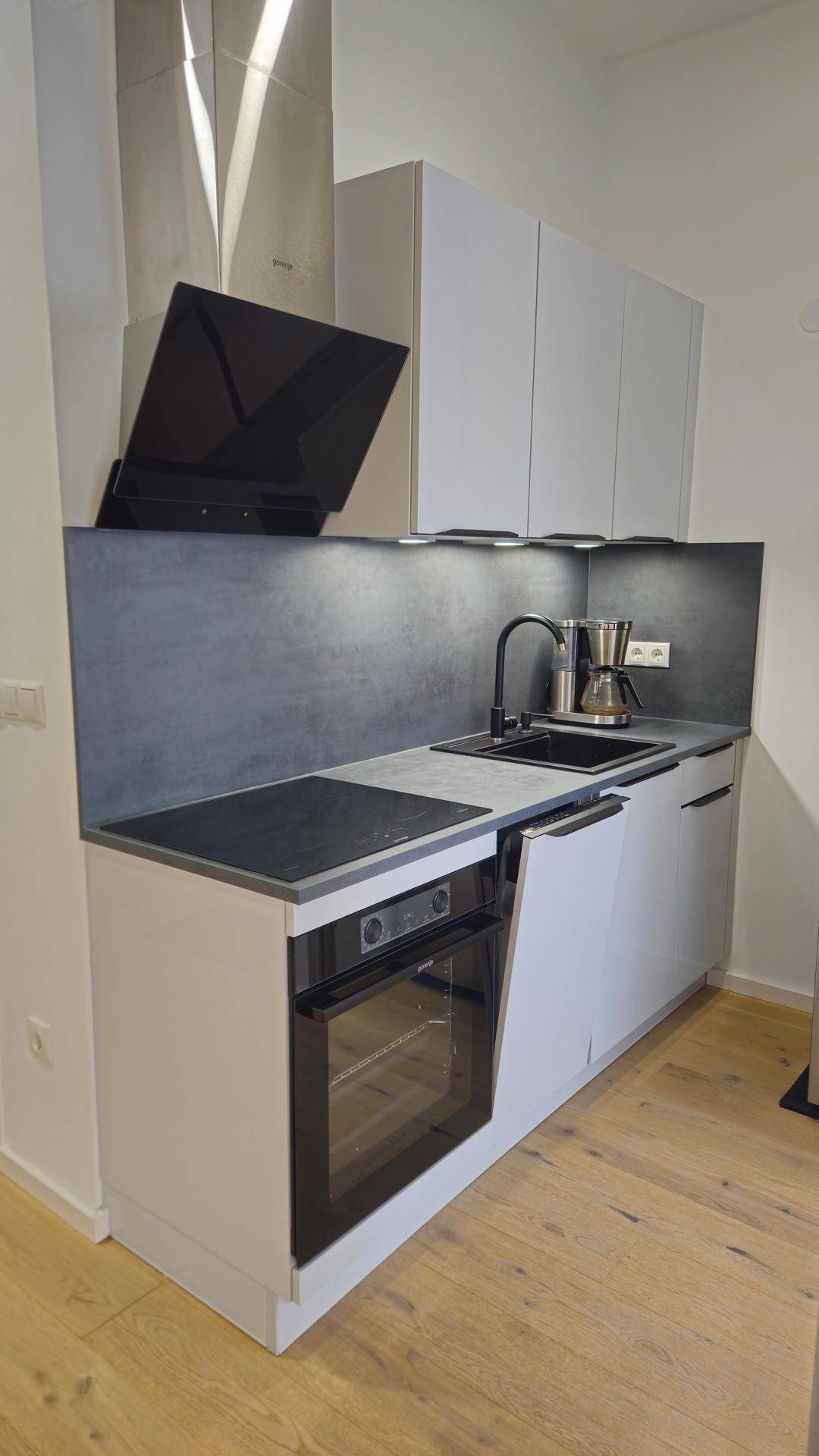Kompakte, moderne Küchenzeile mit weißen Schränken, Induktionskochfeld und integriertem Backofen.