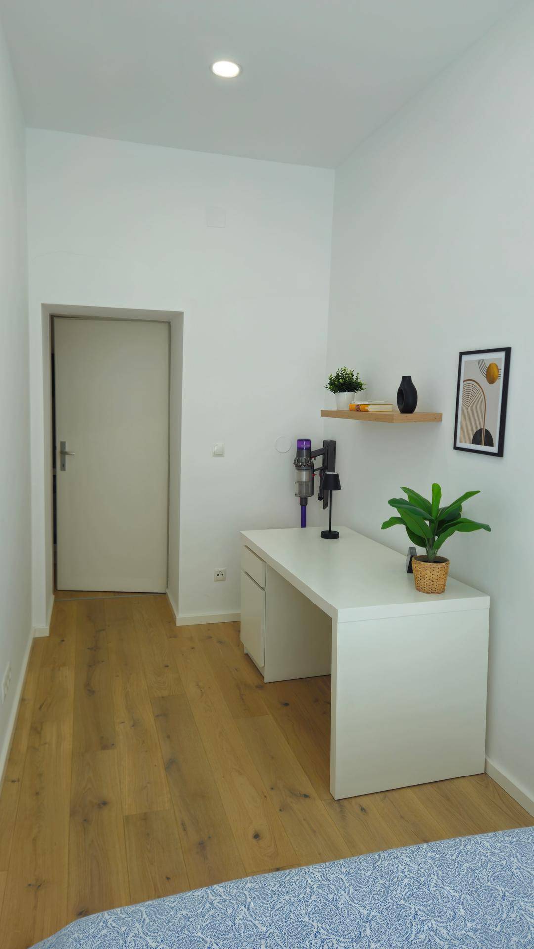Helles Schlafzimmer mit Schreibtisch, Holzboden und einfacher, funktionaler Einrichtung.
