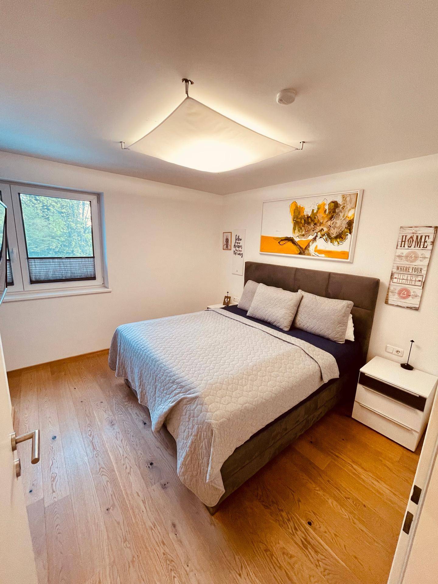 Gemütliches Schlafzimmer mit Doppelbett, Holzboden und Fenster, das viel Tageslicht hereinlässt.