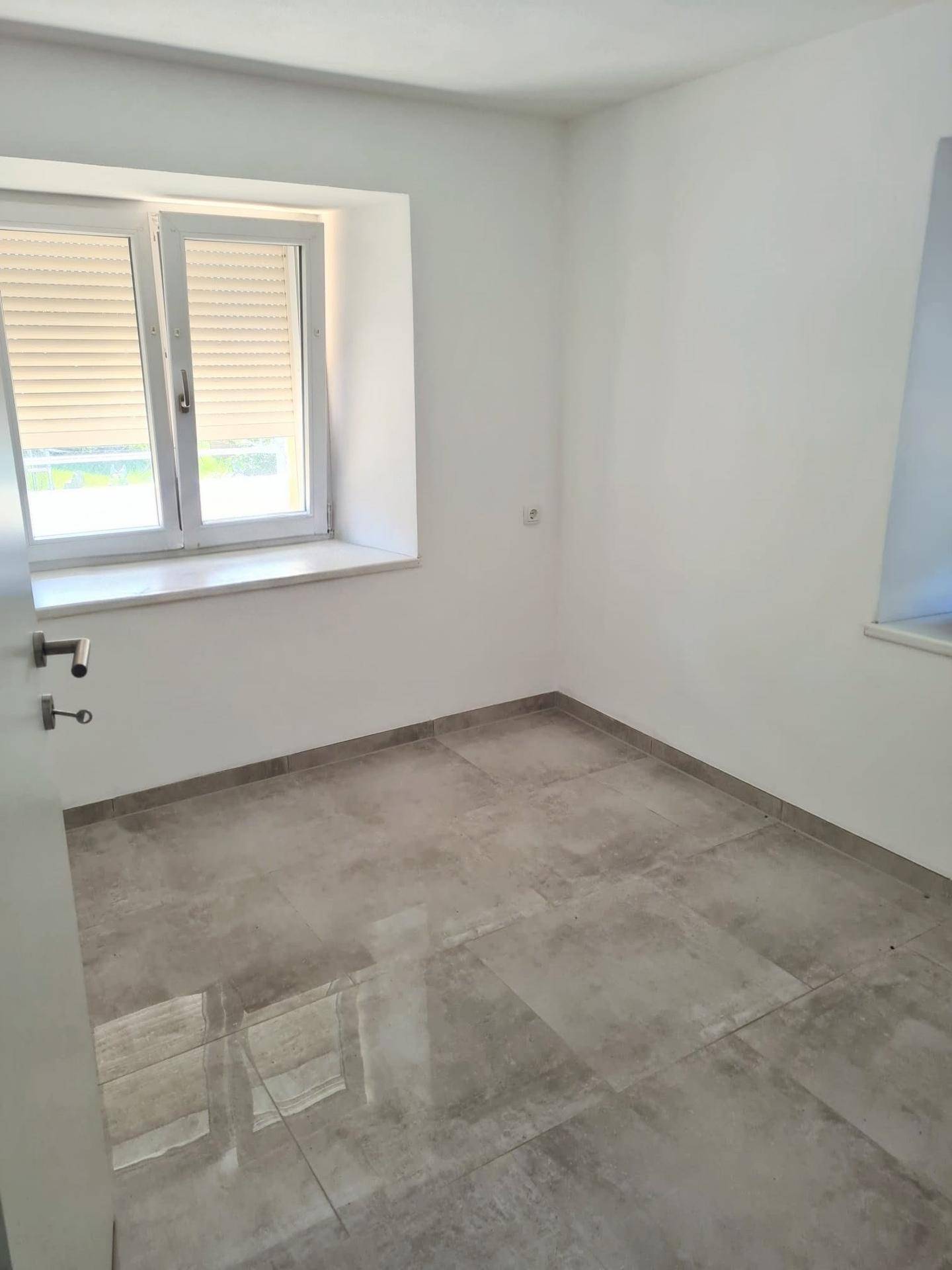Helles Schlafzimmer mit Fliesenboden und Fenster mit Rollläden, bereit zur individuellen Gestaltung.