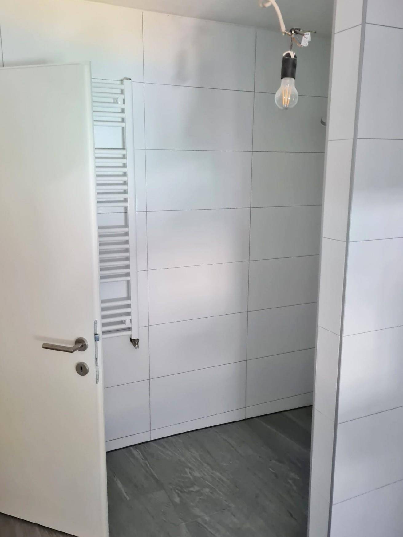 Modern gefliestes Badezimmer mit weißem Handtuchheizkörper und vorbereiteter Duschzone.
