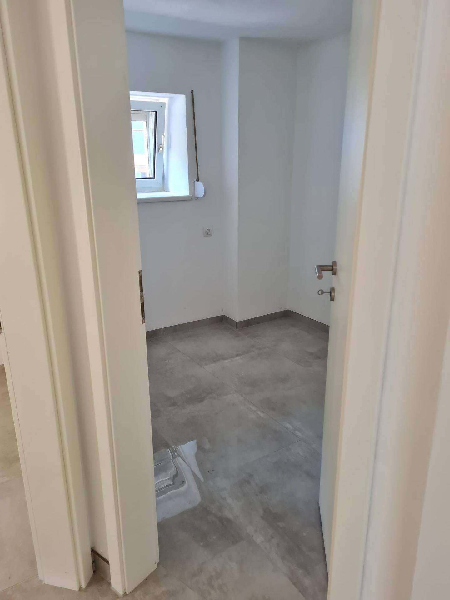 Weiteres helles Schlafzimmer mit Fliesenboden und Fenster, ideal für Gäste oder Kinderzimmer.