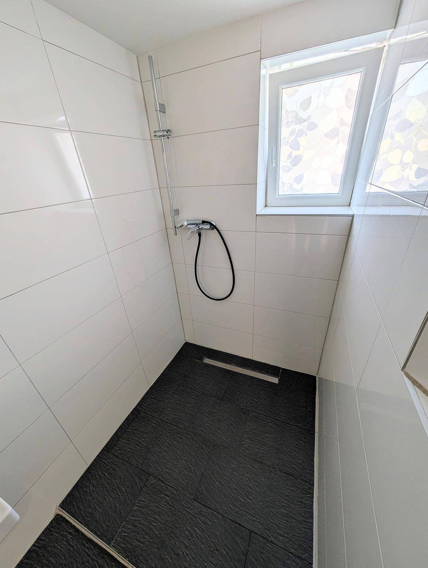 Moderne Duschkabine mit weißen Wandfliesen, dunklem Boden und einem Fenster für Belüftung.