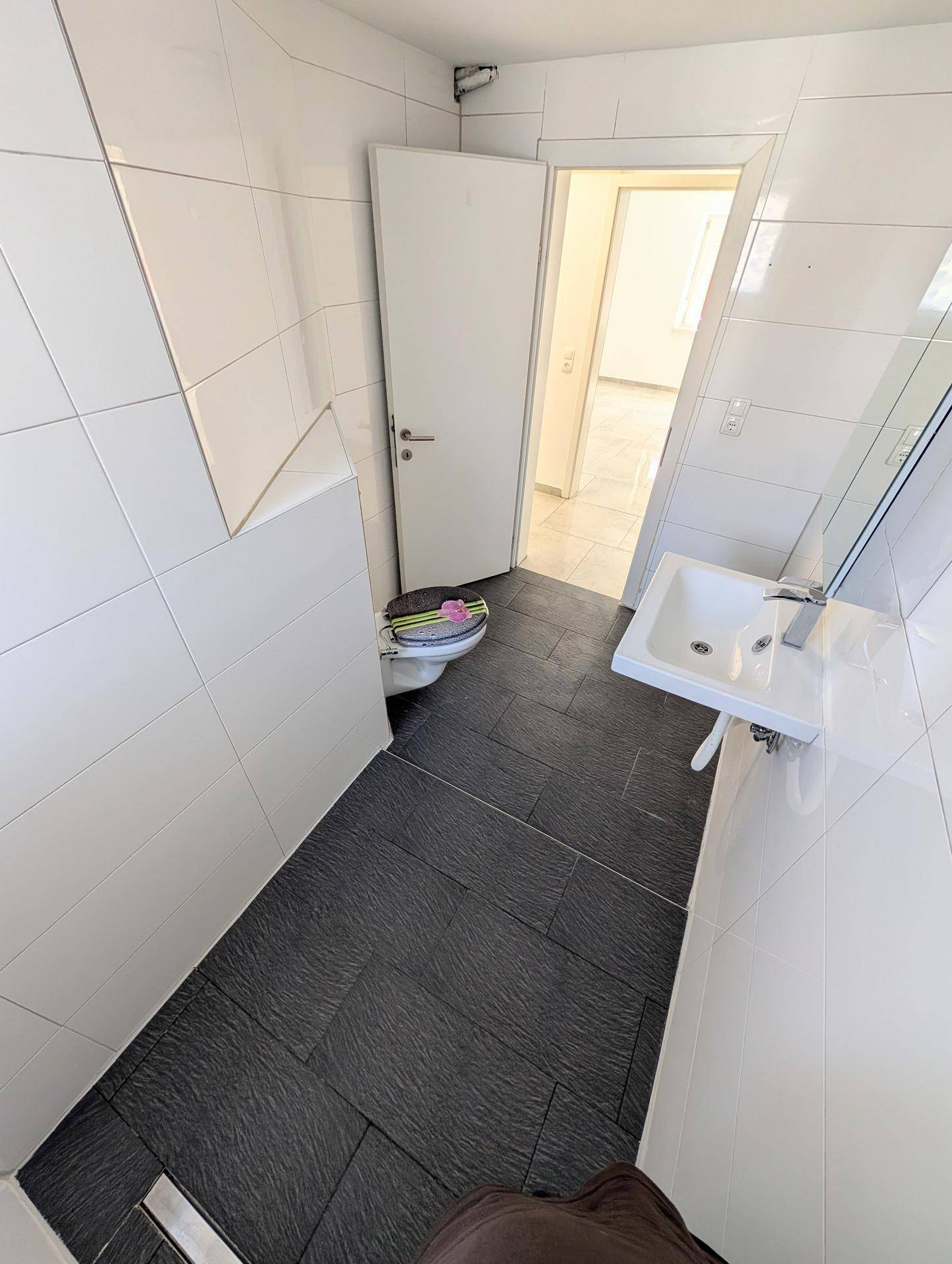 Helles Badezimmer mit WC, Waschbecken und offener Tür, die den Zugang zum nächsten Raum ermöglicht.