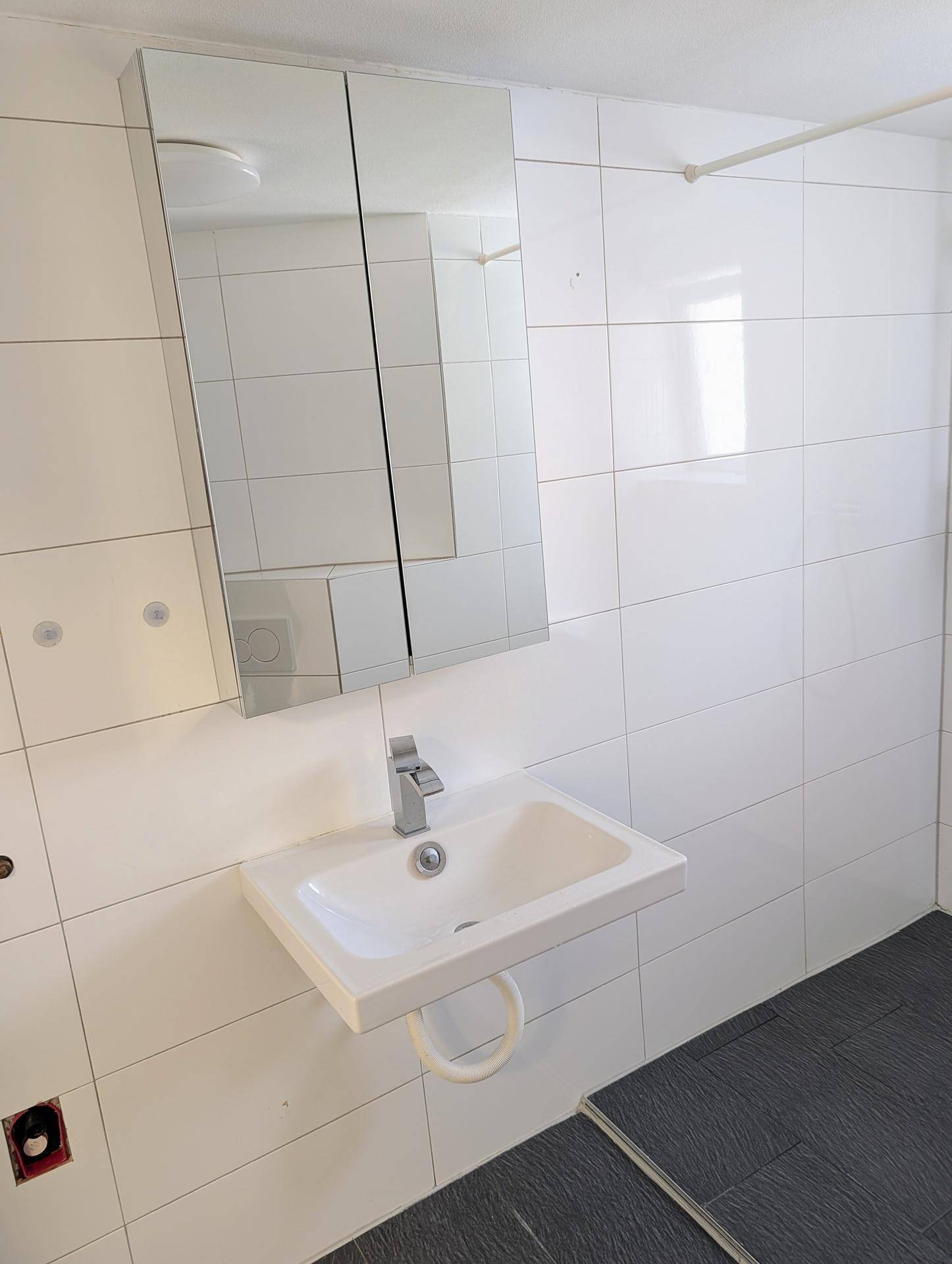 Detailaufnahme des Waschbeckens und des Spiegelschranks in einem hell gefliesten Badezimmer.