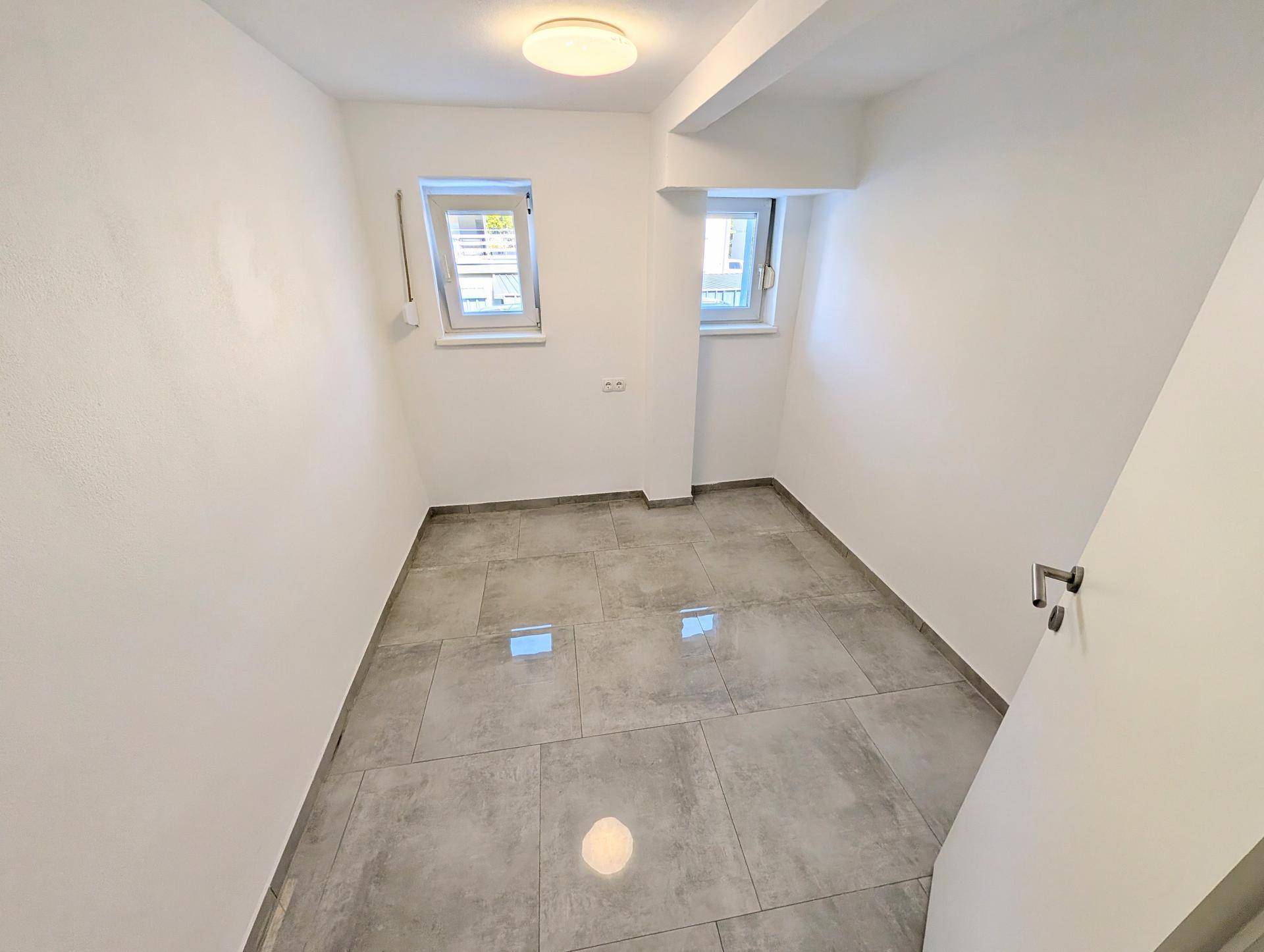 Heller, leerer Raum mit zwei Fenstern und modernen grauen Fliesen, ideal für ein Schlafzimmer.