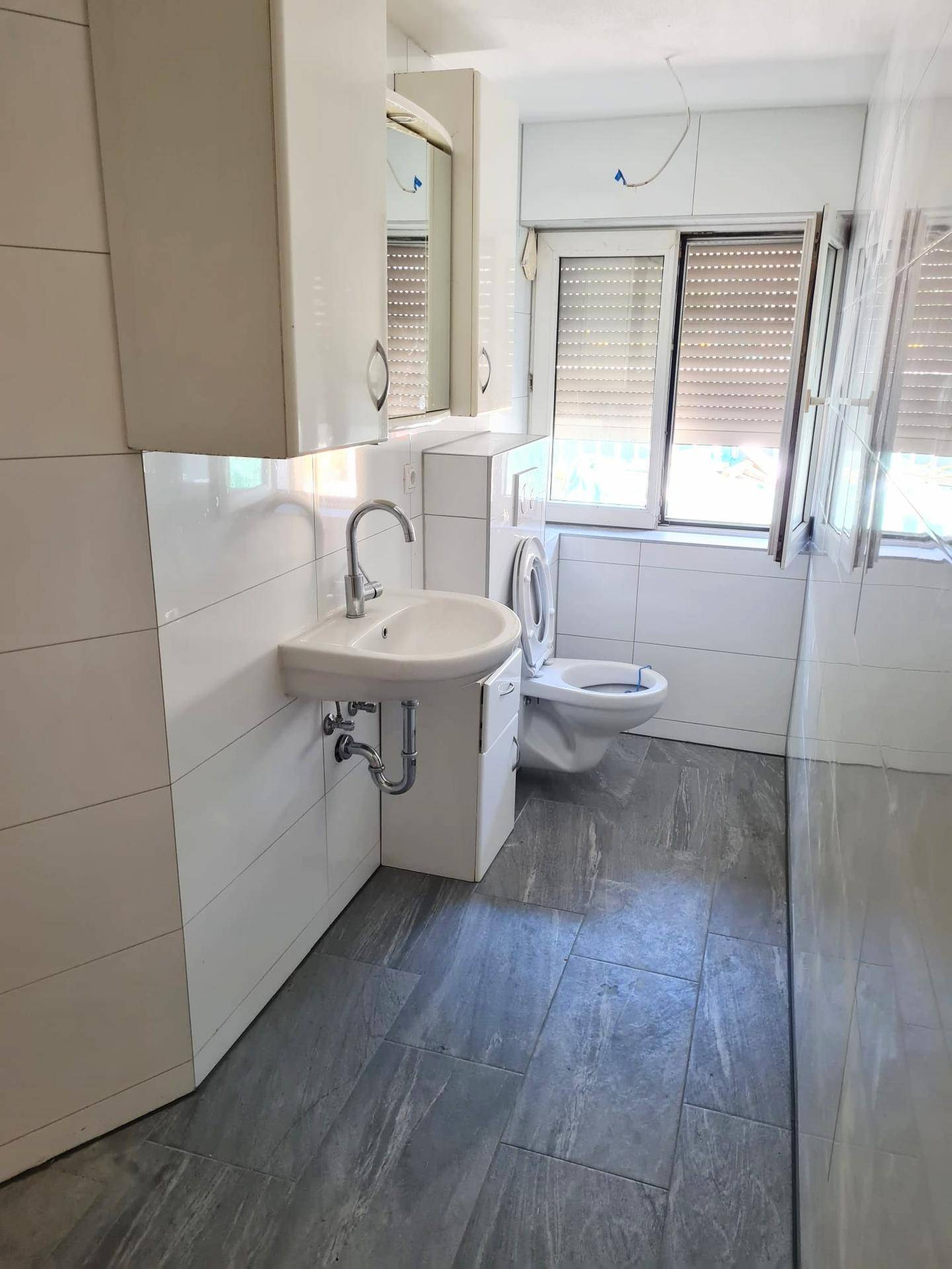 Funktionales Badezimmer mit Waschbecken, WC, Fenster und Anschluss für eine Waschmaschine.