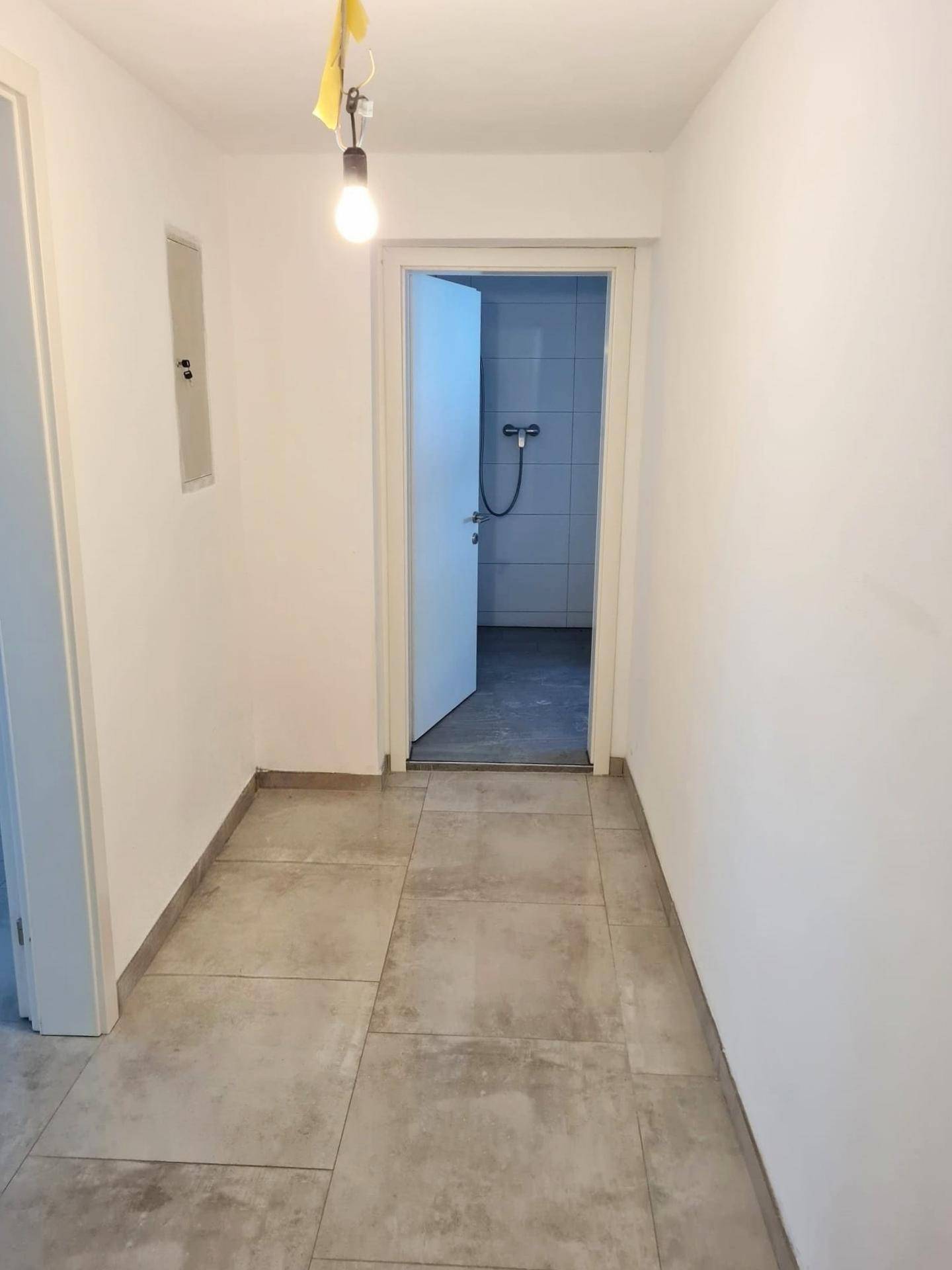Langer Flur mit Fliesenboden und Zugang zu weiteren Räumen, inklusive Badezimmer.