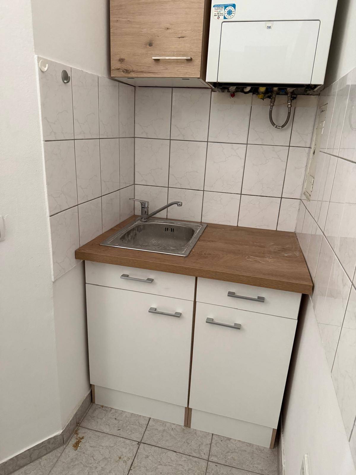 Spülbereich der Küchenzeile mit Waschbecken, Holzoptik-Arbeitsplatte und Wandfliesen, inklusive Warmwasserbereiter.