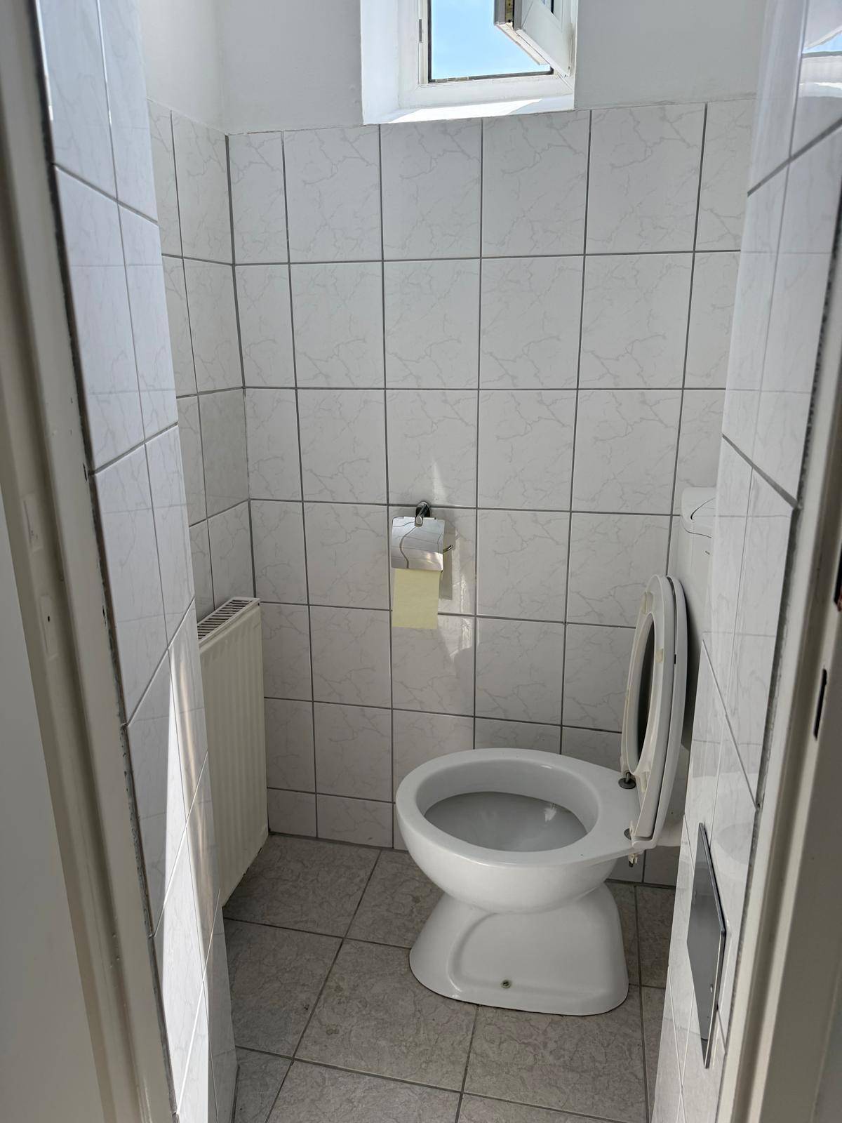 Separates WC mit Fenster, Toilette und weißen Wandfliesen, bietet Privatsphäre und Belüftung.