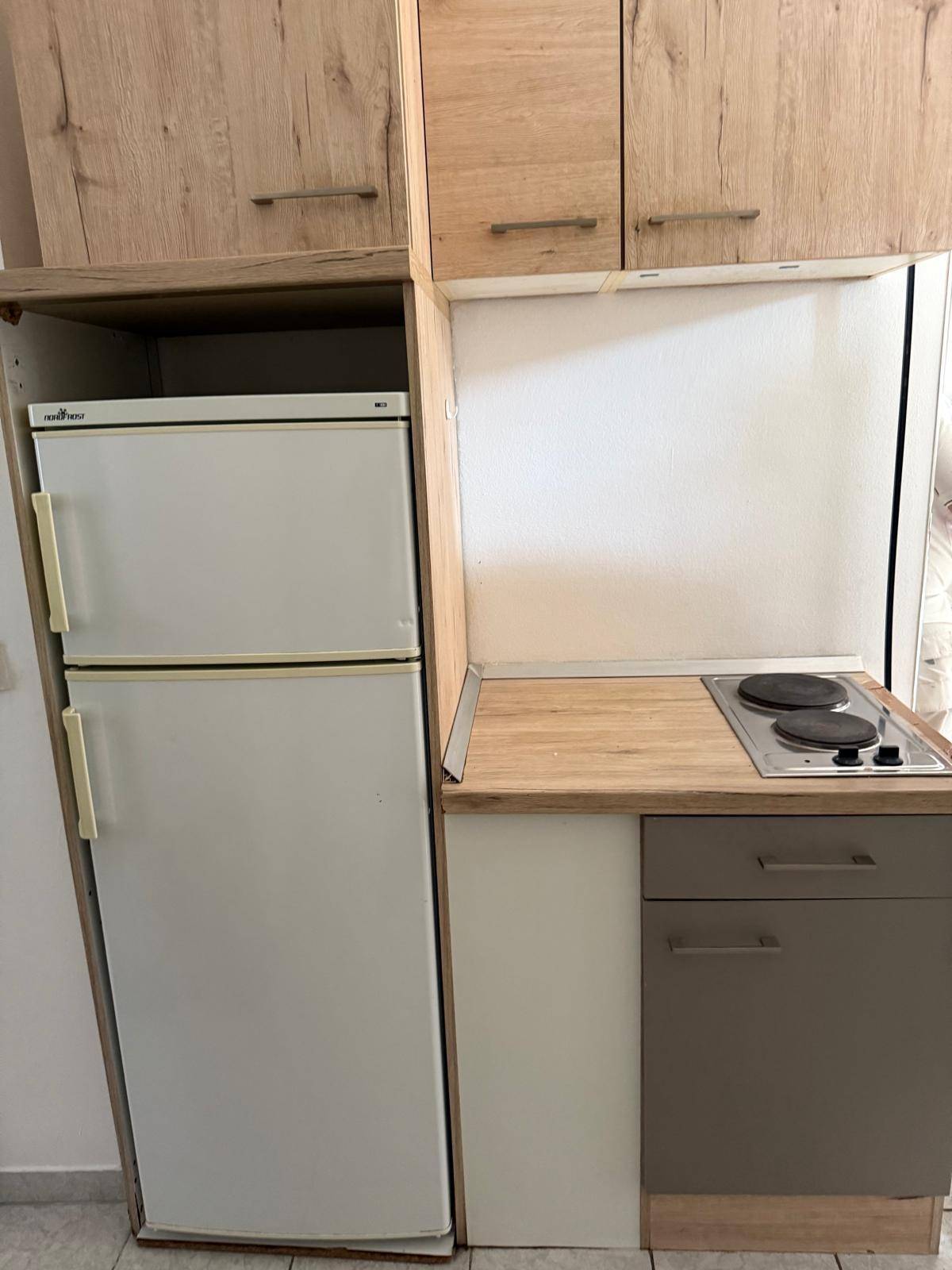 Kompakte Einbauküche mit Kühlschrank, Kochfeld und Holzoptik-Arbeitsplatte, praktisch und funktional.