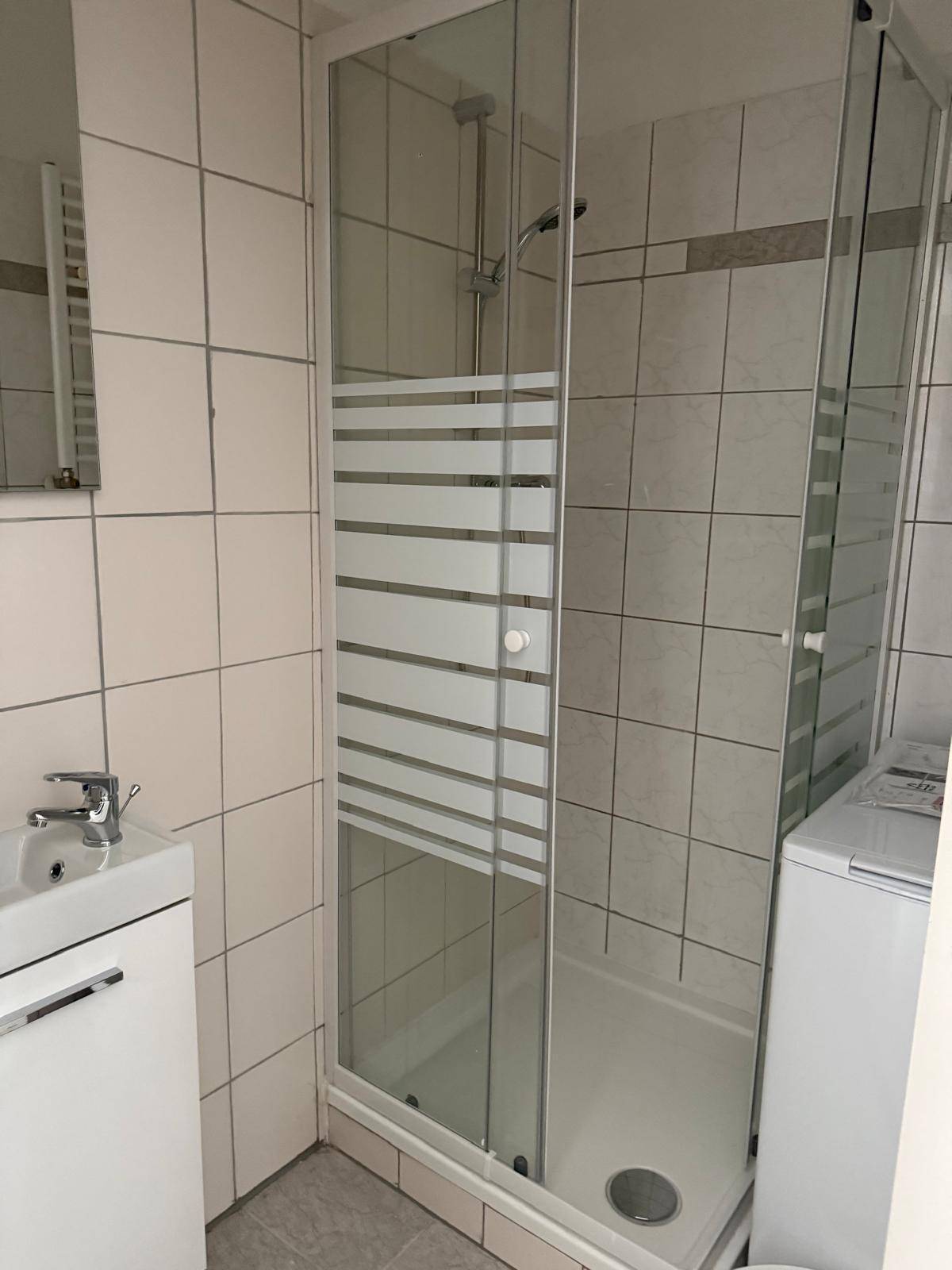 Modernes Badezimmer mit Duschkabine, Waschbecken und hellen Wandfliesen, sauber und funktional gestaltet.