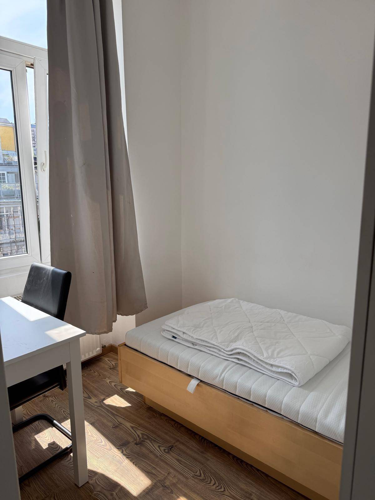 Bettbereich im Schlafzimmer mit Fenster, das viel Tageslicht hereinlässt und einen Blick nach draußen bietet.