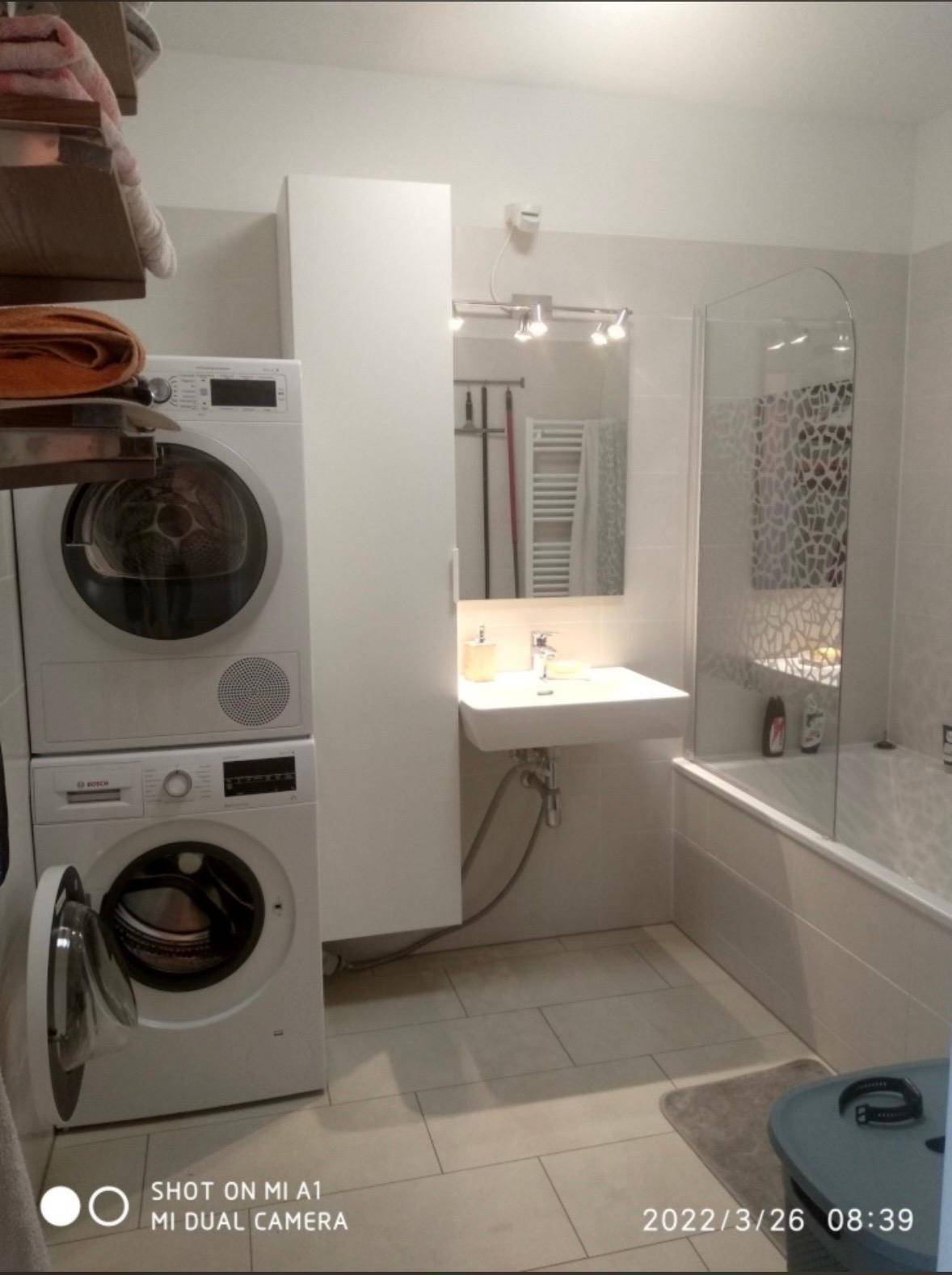 Modernes Badezimmer mit Badewanne, Waschbecken und integrierter Waschmaschine und Trockner.