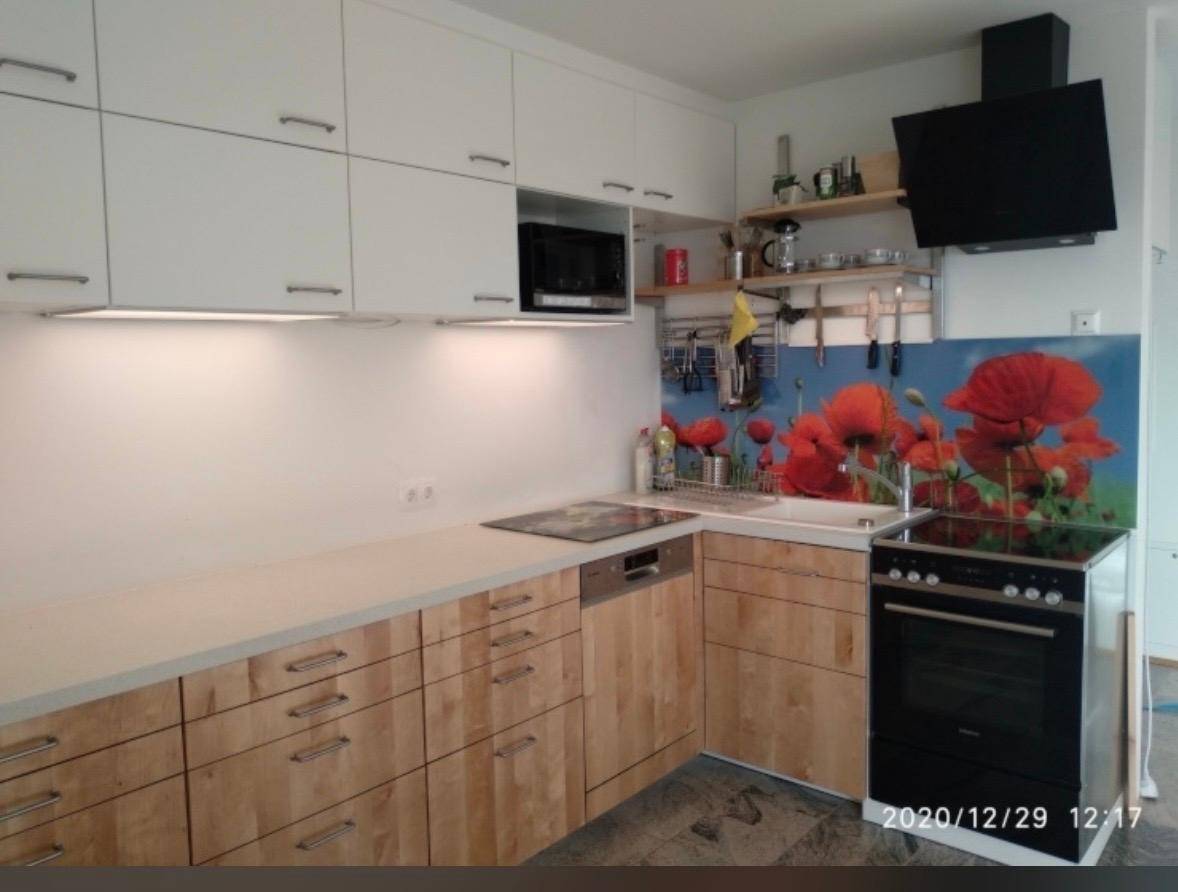 Moderne Küche mit hellen Holzfronten, weißen Oberschränken und floraler Rückwand.