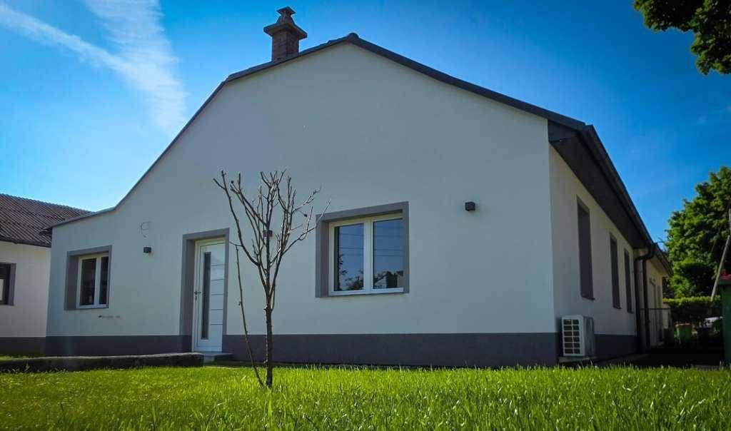 Rückansicht des Einfamilienhauses mit weißer Fassade, Satteldach und einem jungen Baum im Garten.