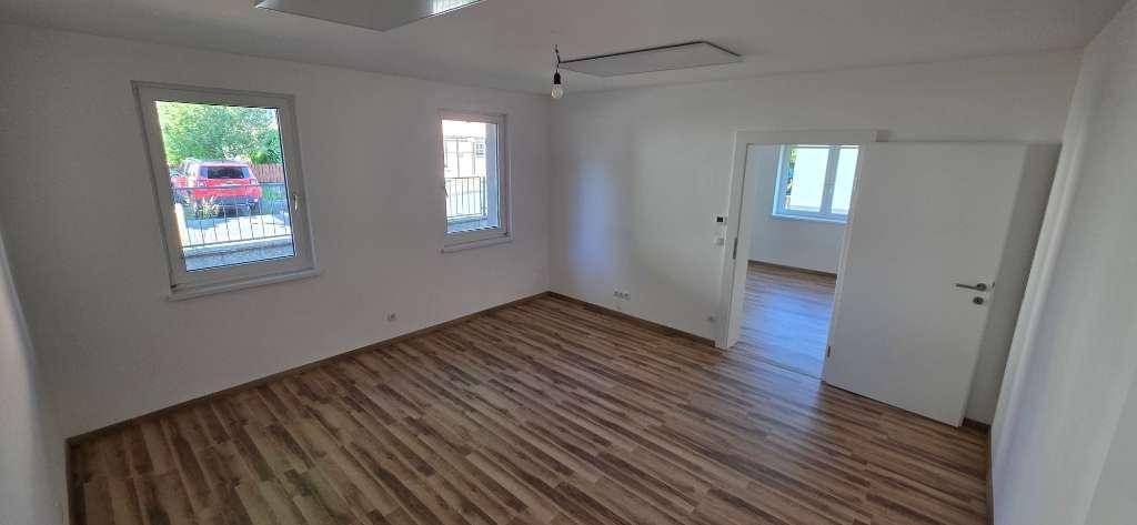 Helles Zimmer mit Holzboden und mehreren Fenstern, das viel Tageslicht hereinlässt.