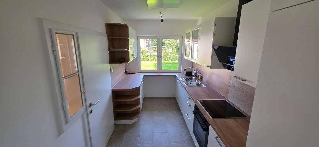 Moderne Küche mit Holztheke, weißen Schränken und einem Fenster mit Blick ins Grüne.