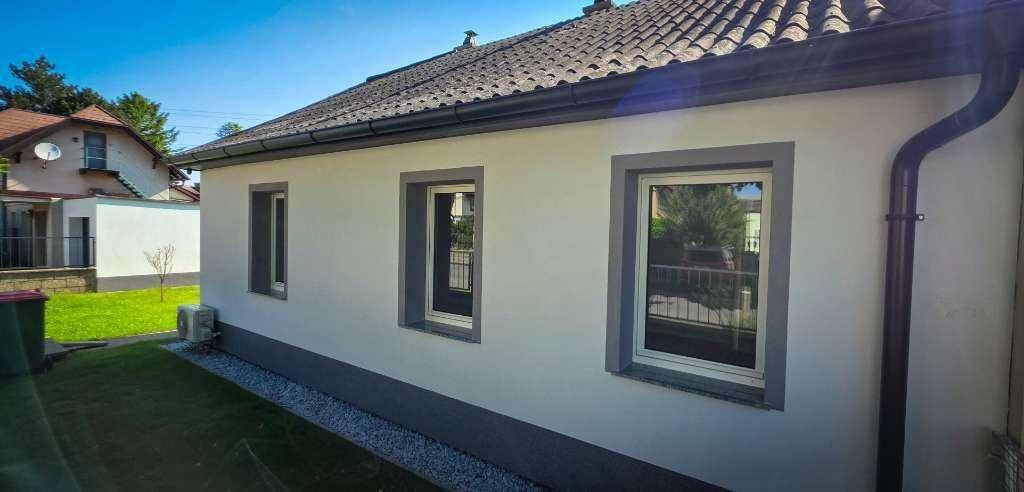 Nahaufnahme der Hausfassade mit modernen Fenstern und dunklen Dachrinnen unter klarem Himmel.