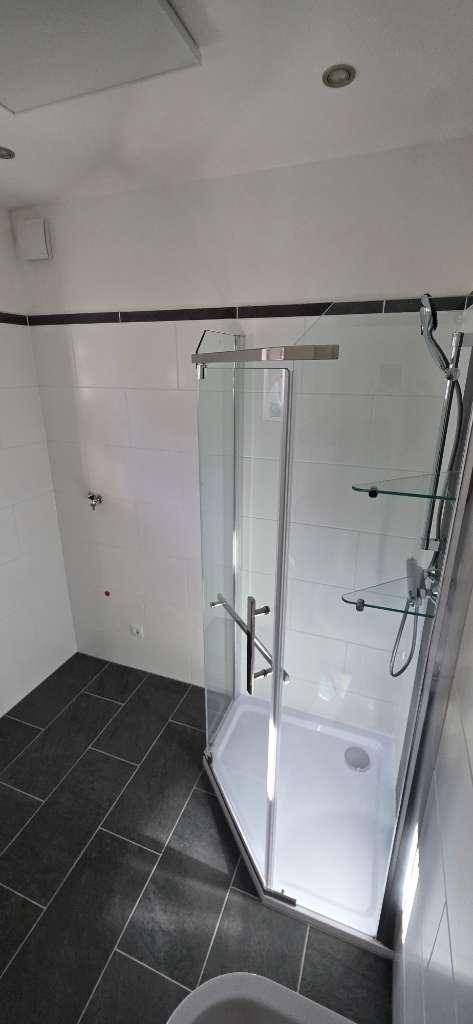 Modernes Badezimmer mit Duschkabine, weißen Wandfliesen und dunklem Fliesenboden.