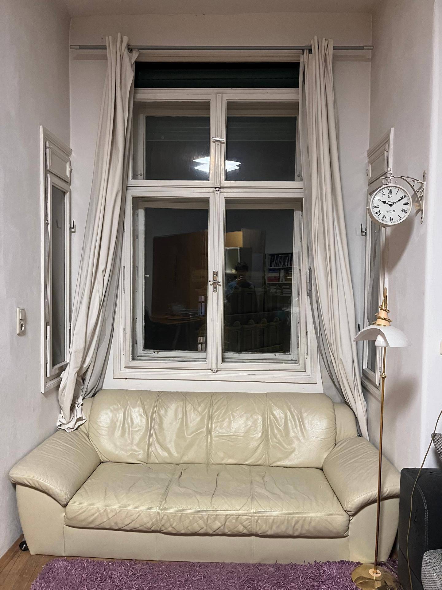 Gemütliche Sitzecke mit hellem Sofa vor einem großen Fenster und Stehlampe.
