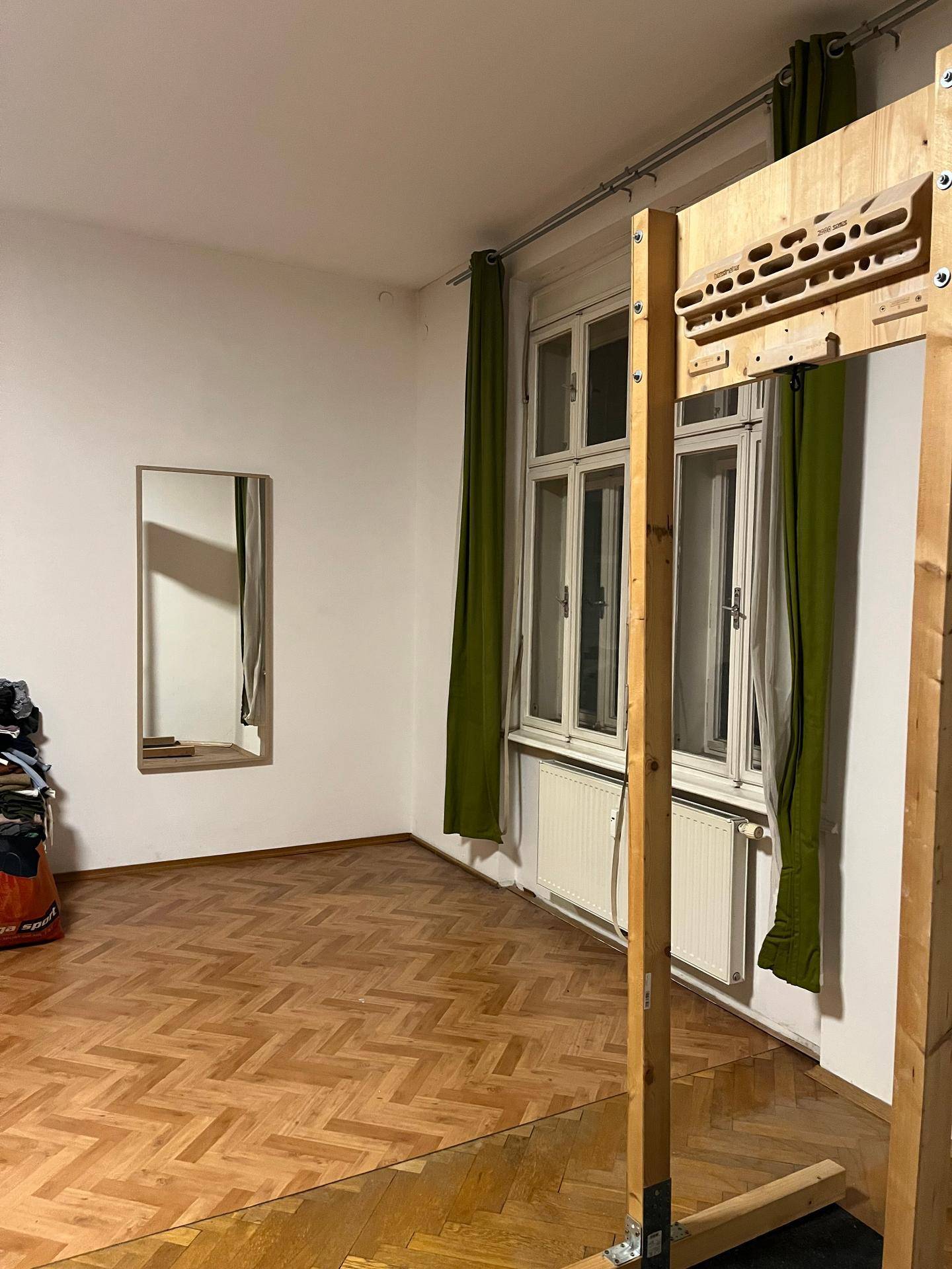 Heller Raum mit Fischgrätparkett, großen Fenstern und einem Trainingsgerät.