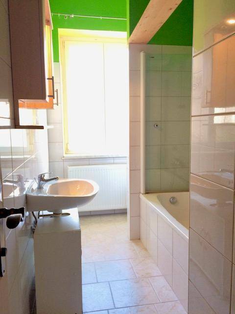 Helles Badezimmer mit weißen Fliesen, Badewanne, Waschbecken und einem Fenster.