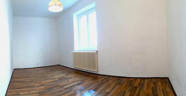 Leerer Raum mit hellen Wänden, einem Fenster, Heizkörper und Holzboden.