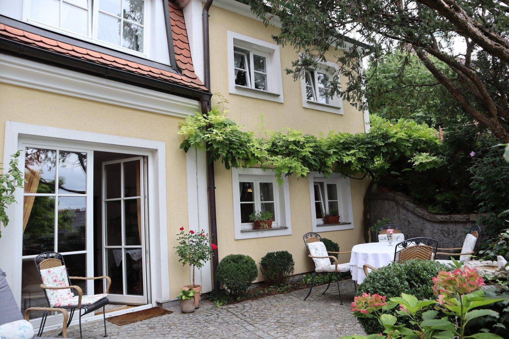 Gemütliche Terrasse mit Gartenmöbeln und üppiger Bepflanzung vor dem Haus.
