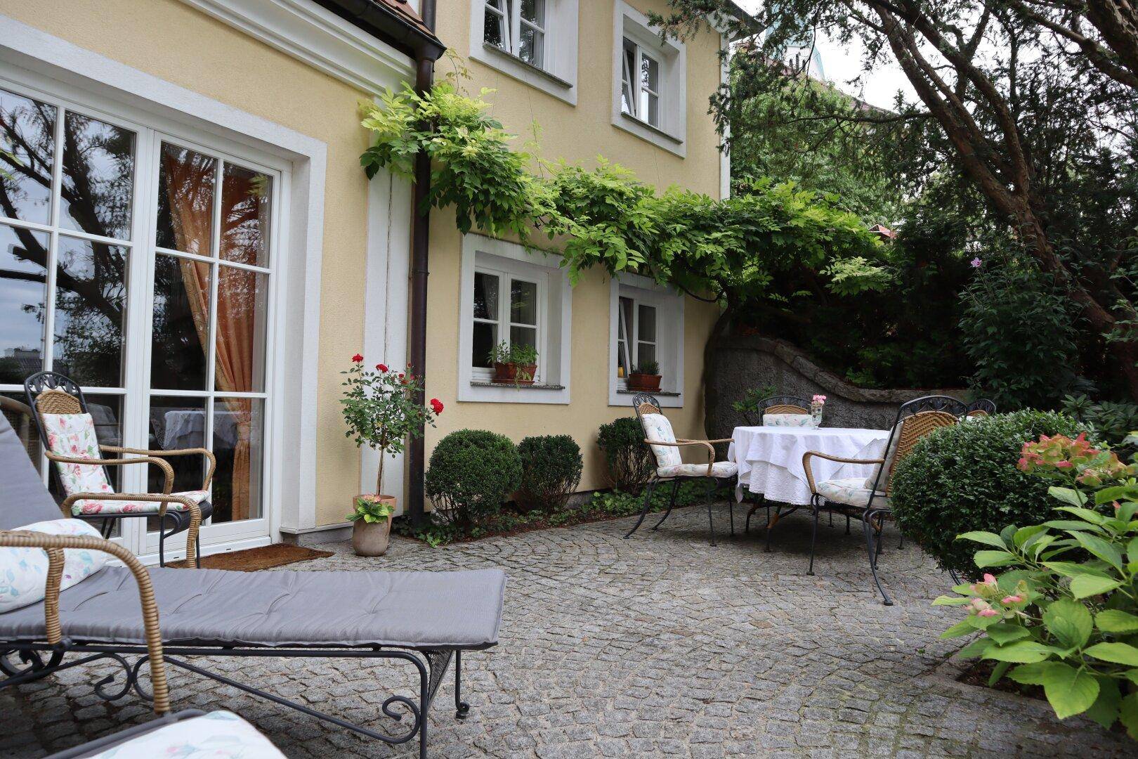 Geräumige Terrasse mit Liegestuhl und Sitzgruppe, umgeben von Grün.